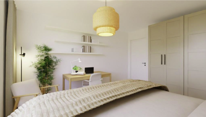 A bright bedroom with a bed, a desk with a chair, shelves with books, a tall floor lamp, a potted plant, a wardrobe, and a hanging light fixture.