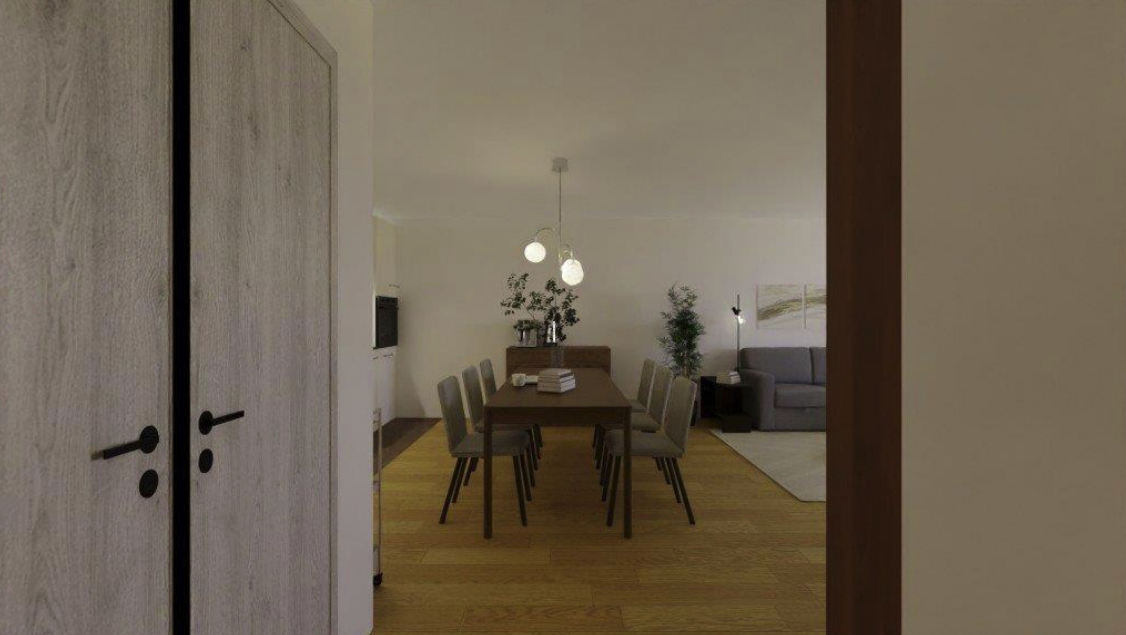 Dining area with a large wooden table, eight chairs, and a sideboard with plants in the background. Adjacent living space with a gray sofa, side table with a lamp, and wall art. Hardwood flooring throughout.