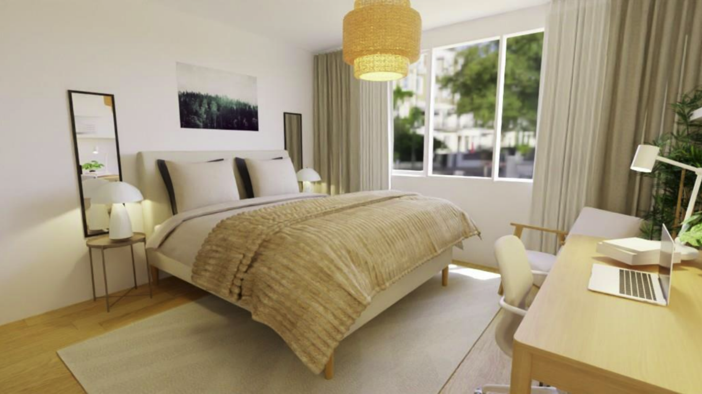 Bright bedroom with a large bed, beige bedding, two nightstands with lamps, a desk with a laptop, white chair, and large window with curtains revealing trees outside.