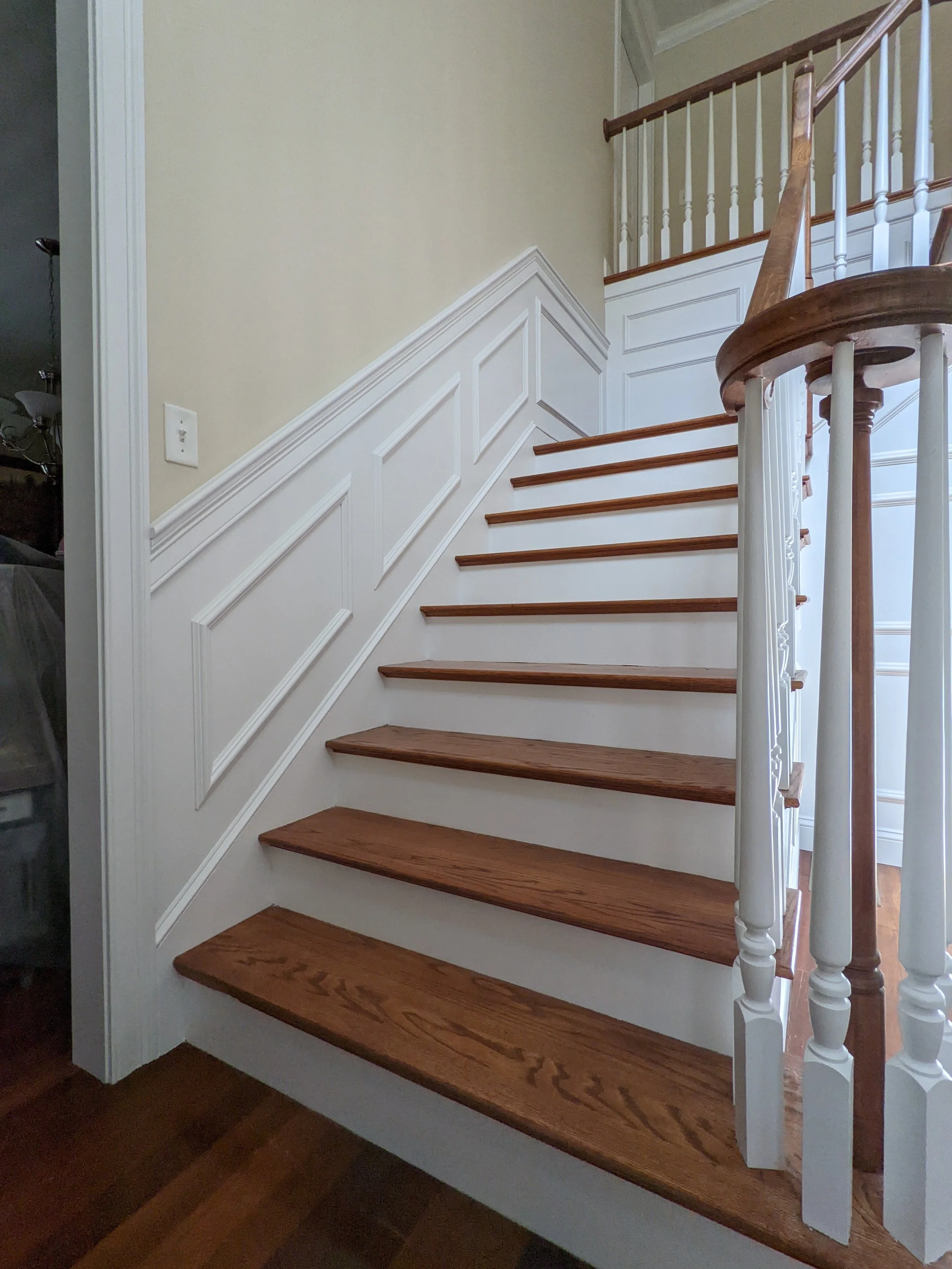 Wooden staircase with white spindle balusters, a white wainscot wall with decorative molding, and beige walls.