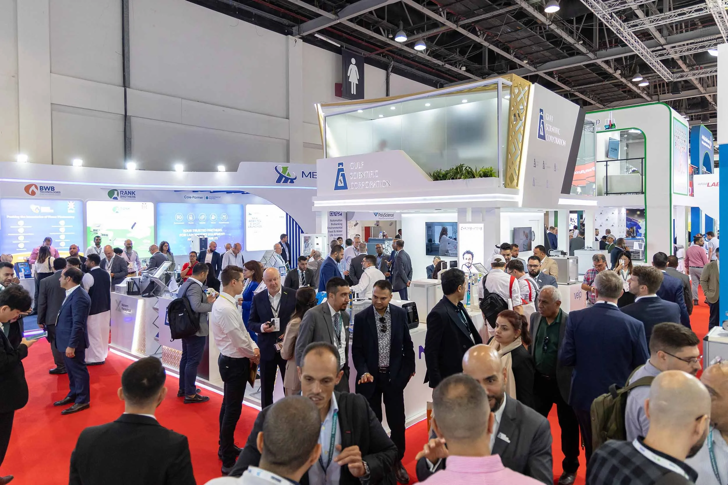Corporate exhibition event photography in Dubai featuring attendees networking around branded exhibition stands at a trade show