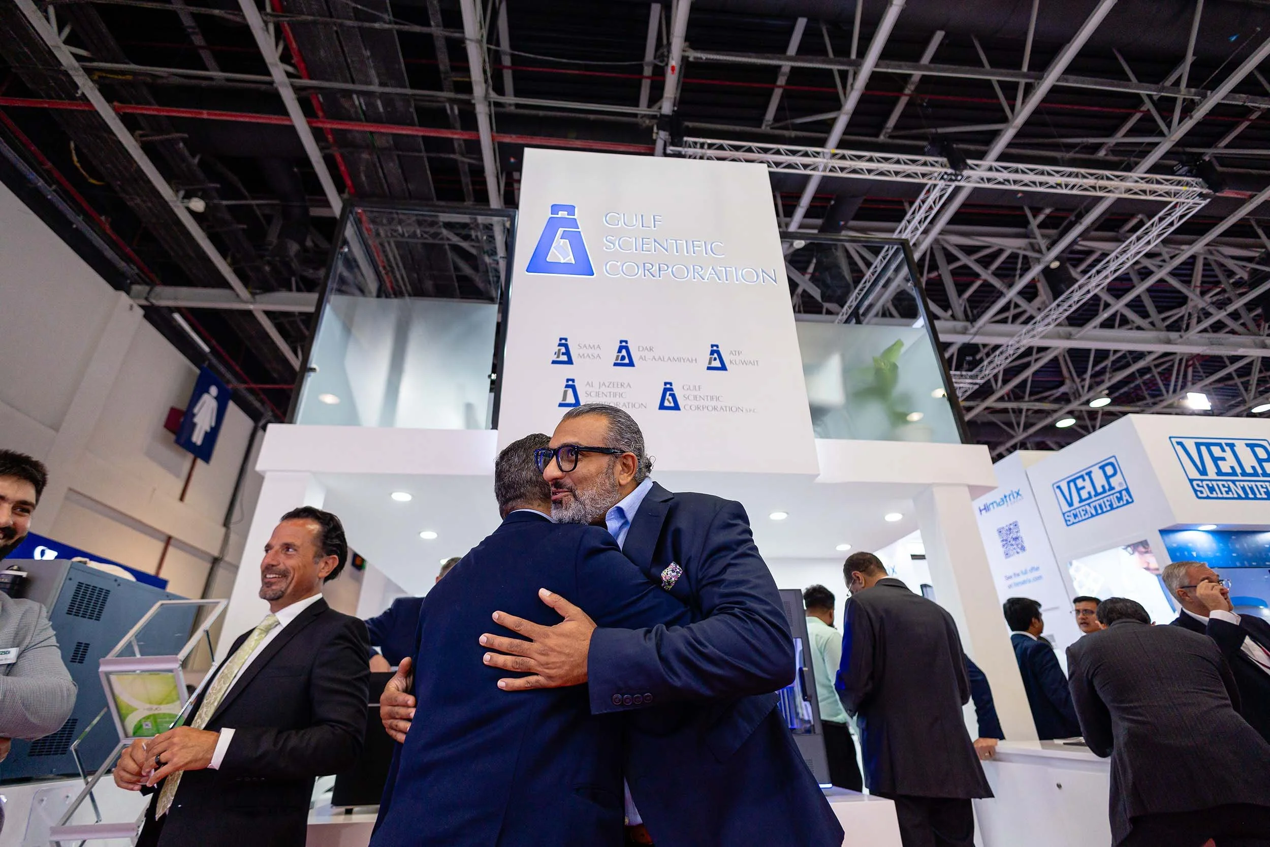Business professionals networking and greeting visitors at the Gulf Scientific exhibition stand during a trade show in Dubai.