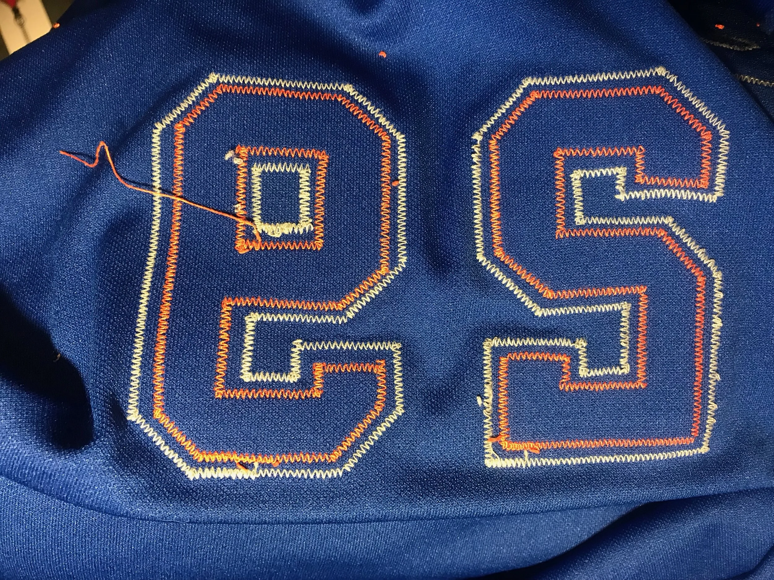 The numbers have been inconveniently sewn through the fabric with both layers. This makes them twice as hard to remove. The old thread was as tough as fishing line after so many exposures to harsh detergents