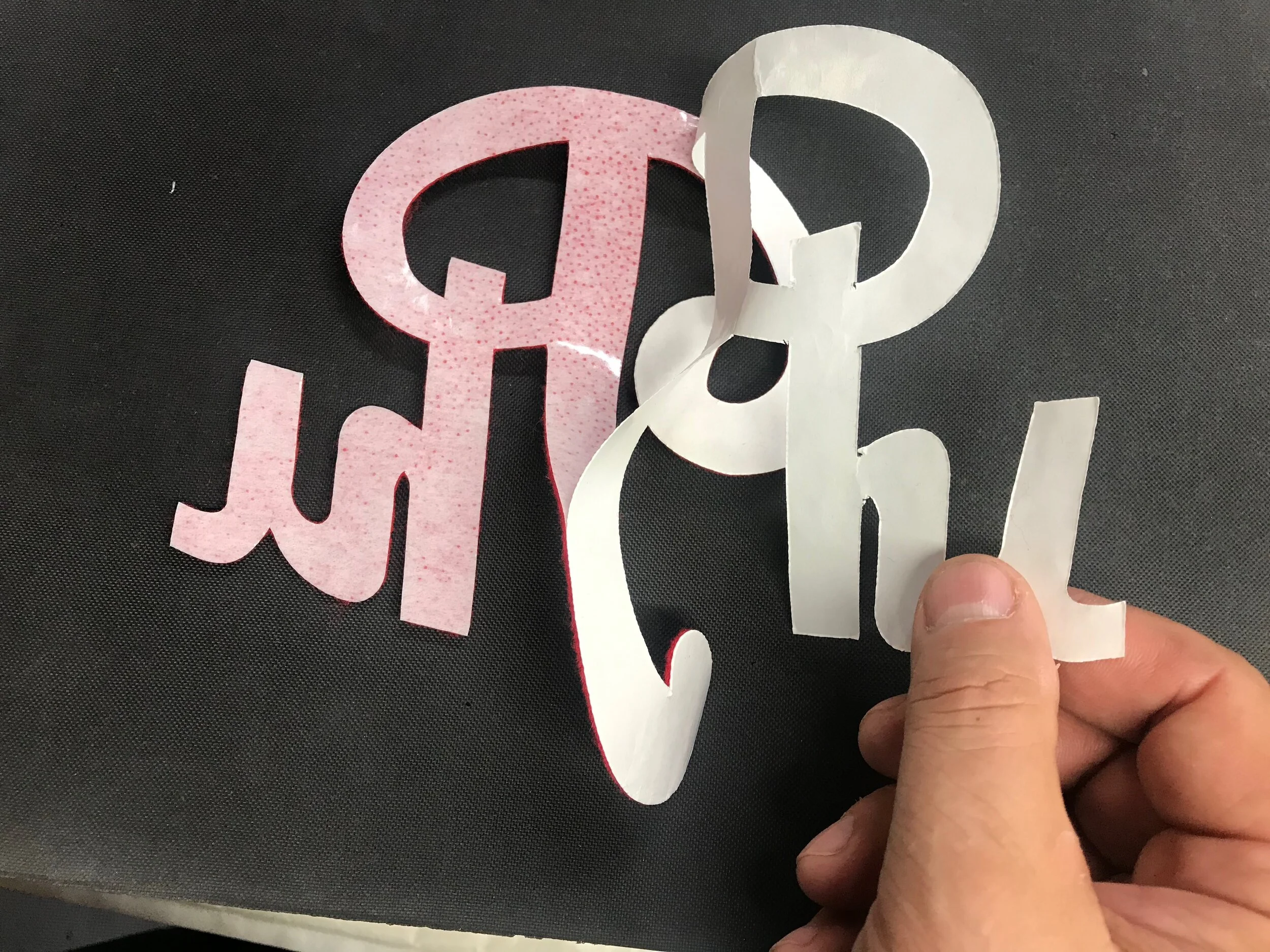 I cut the lettering from the back, right through the paper backing of the film. Once the appliques are cut, I peel off the backing paper exposing the heat-sensitive plastic film below.