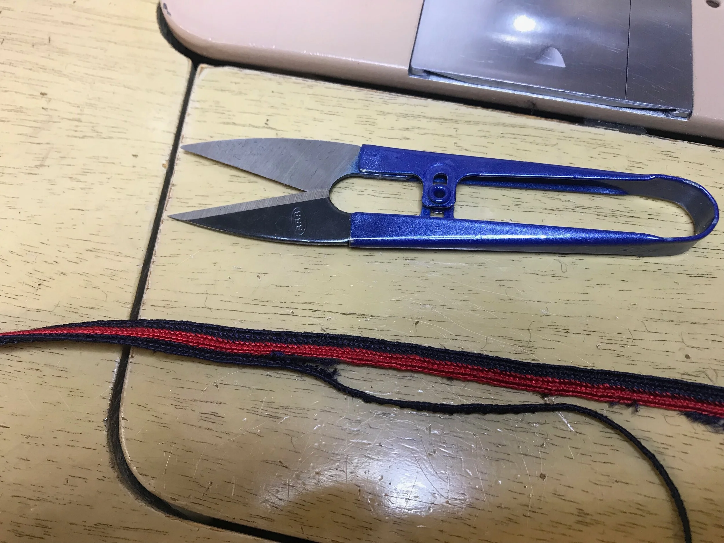 All of the trim had to come off the jersey, a stitch at time.

Then, working slowly and carefully, I snipped the woven edge off the ribbon and un-wove it, leaving perfect two-color, navy and crimson trim.