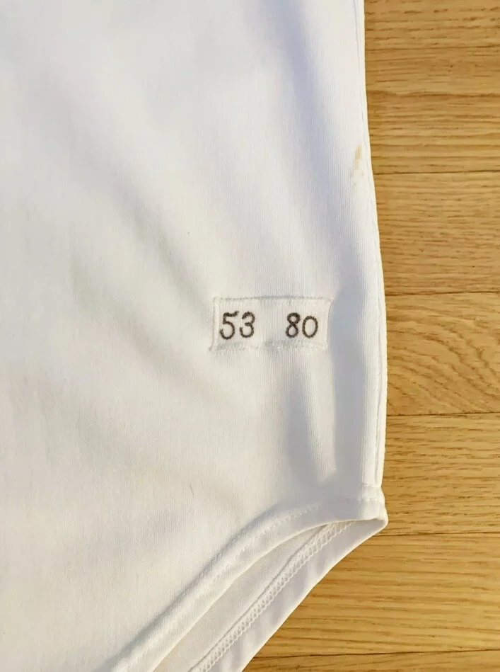 On the outside left tail is a rectangle of knit fabric with “53 80." The tag decodes to player number 53, 1980. The tag is zig zag stitched to the tail, and a careful examination of the tag and its stitching on the light table allow me to conclude th