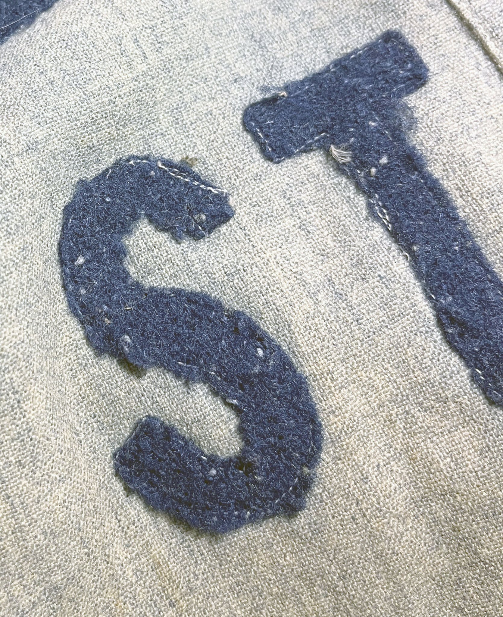 The front lettering here is chain stitched onto pieces of white linen, and then the linen was cut into the letters to spell the words, and they were straight stitched onto the jersey with white cotton thread. No player numbers were on the back; that 