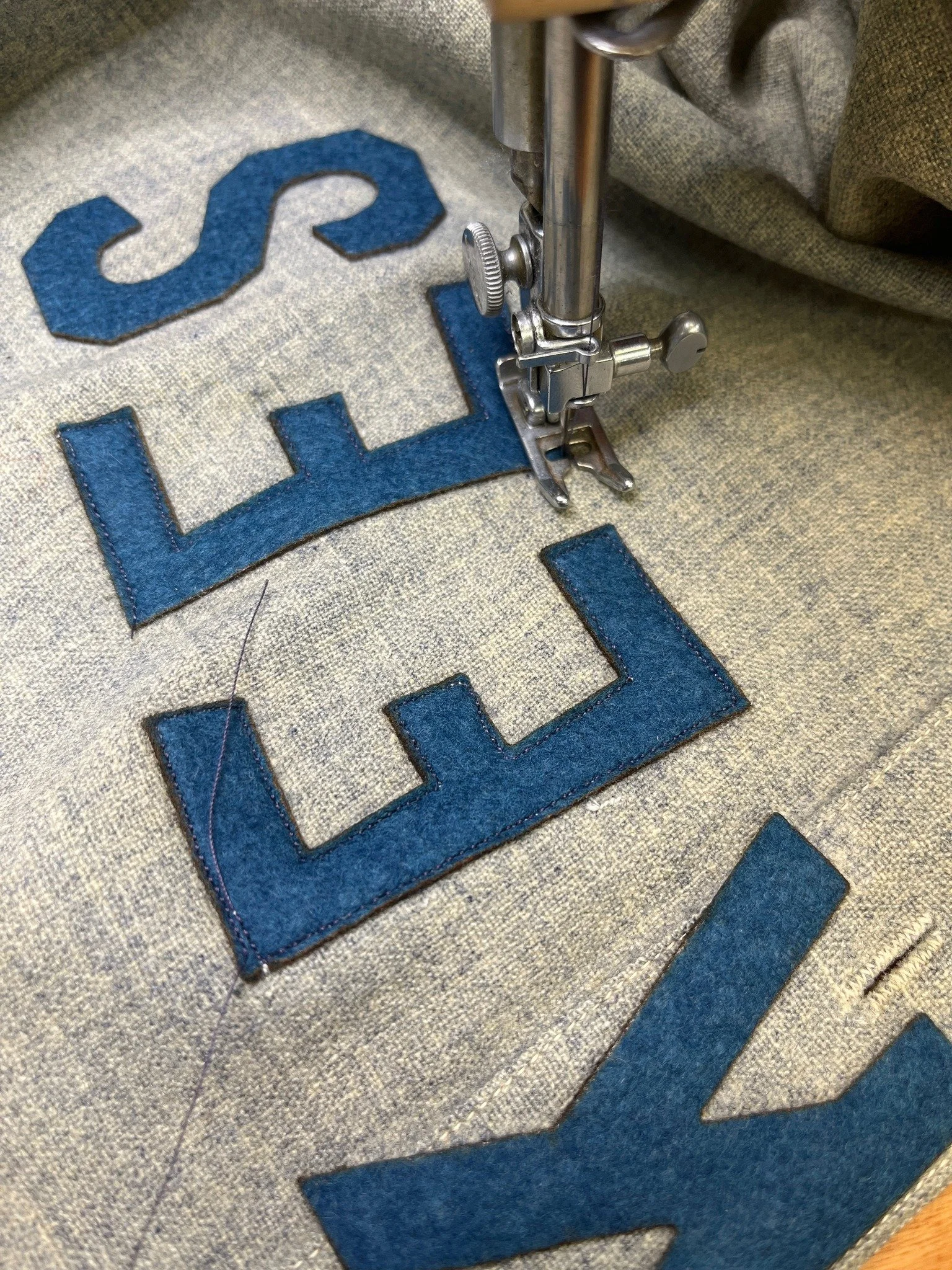 Now, with the jersey back on the light table, I position the letters precisely over the ghosts of a century ago, and tack them down with a light adhesive. Using a straight stitch and period-cotton thread bleached purple (the thread color is called “e