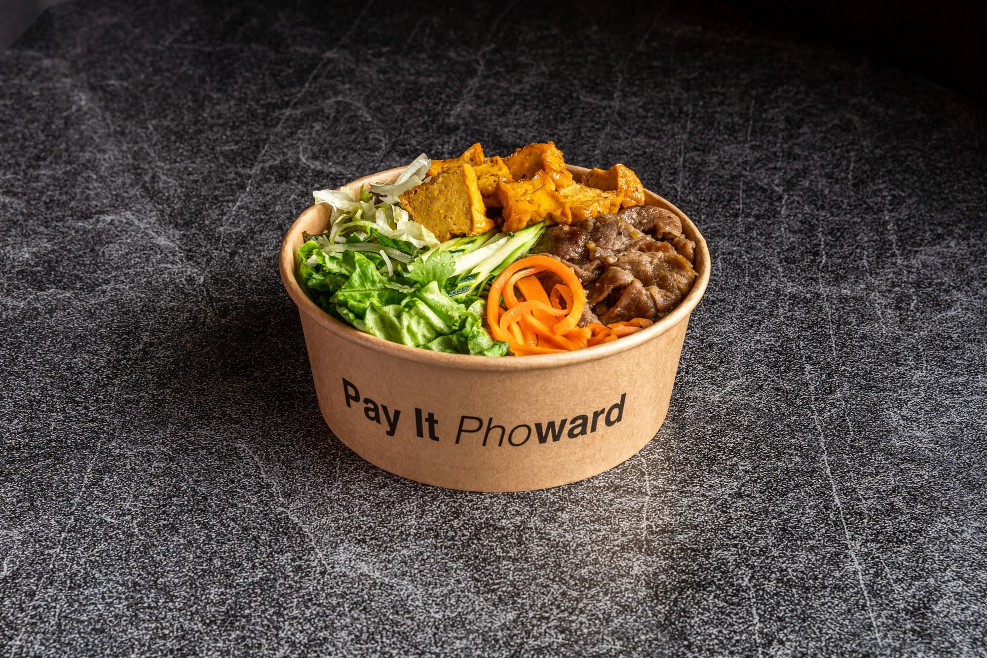 Takeout container with mixed salad, grilled beef, and tofu on black countertop.