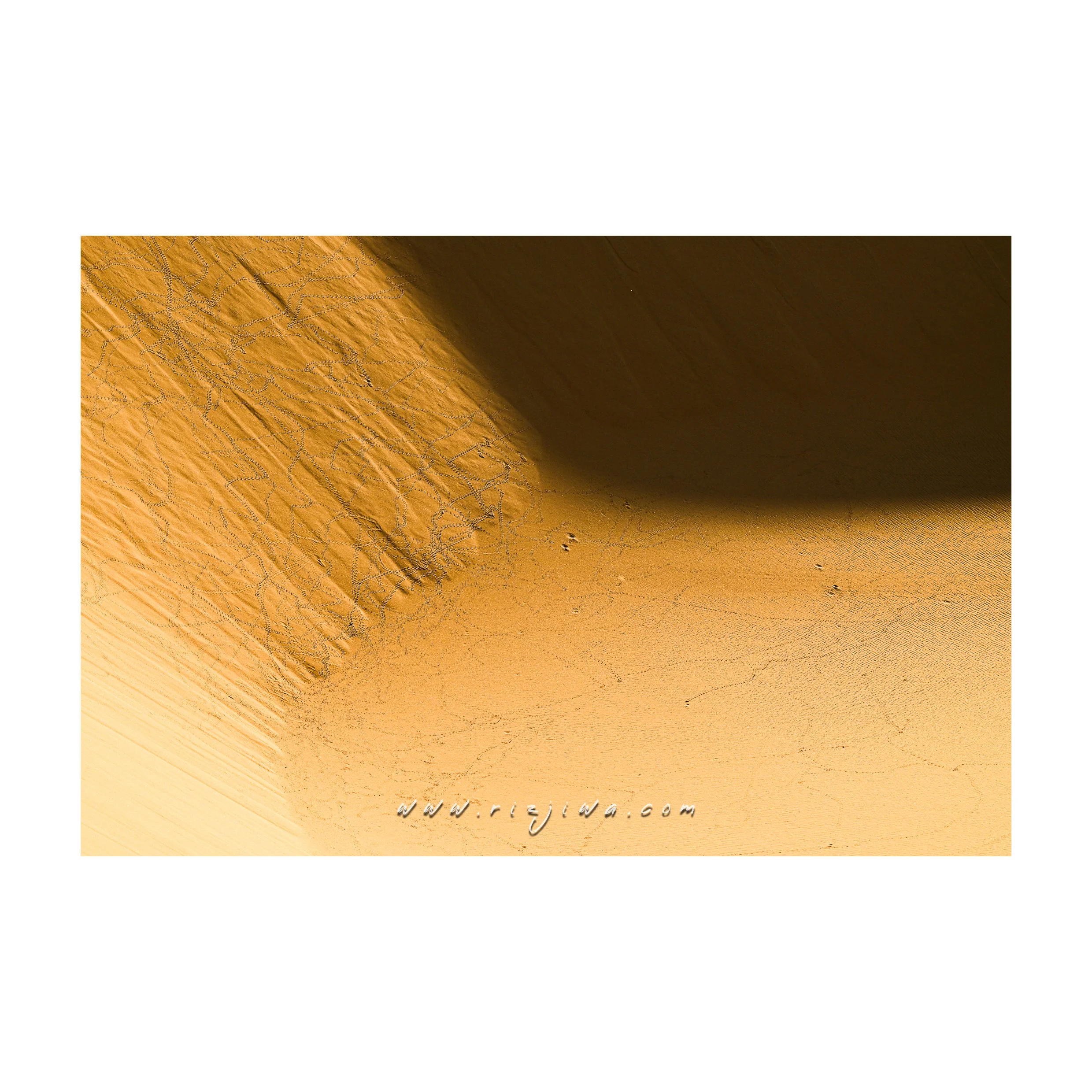 Close-up of a sand dune in a desert with a shadow casting across it, showing ripples and cracks in the sand.