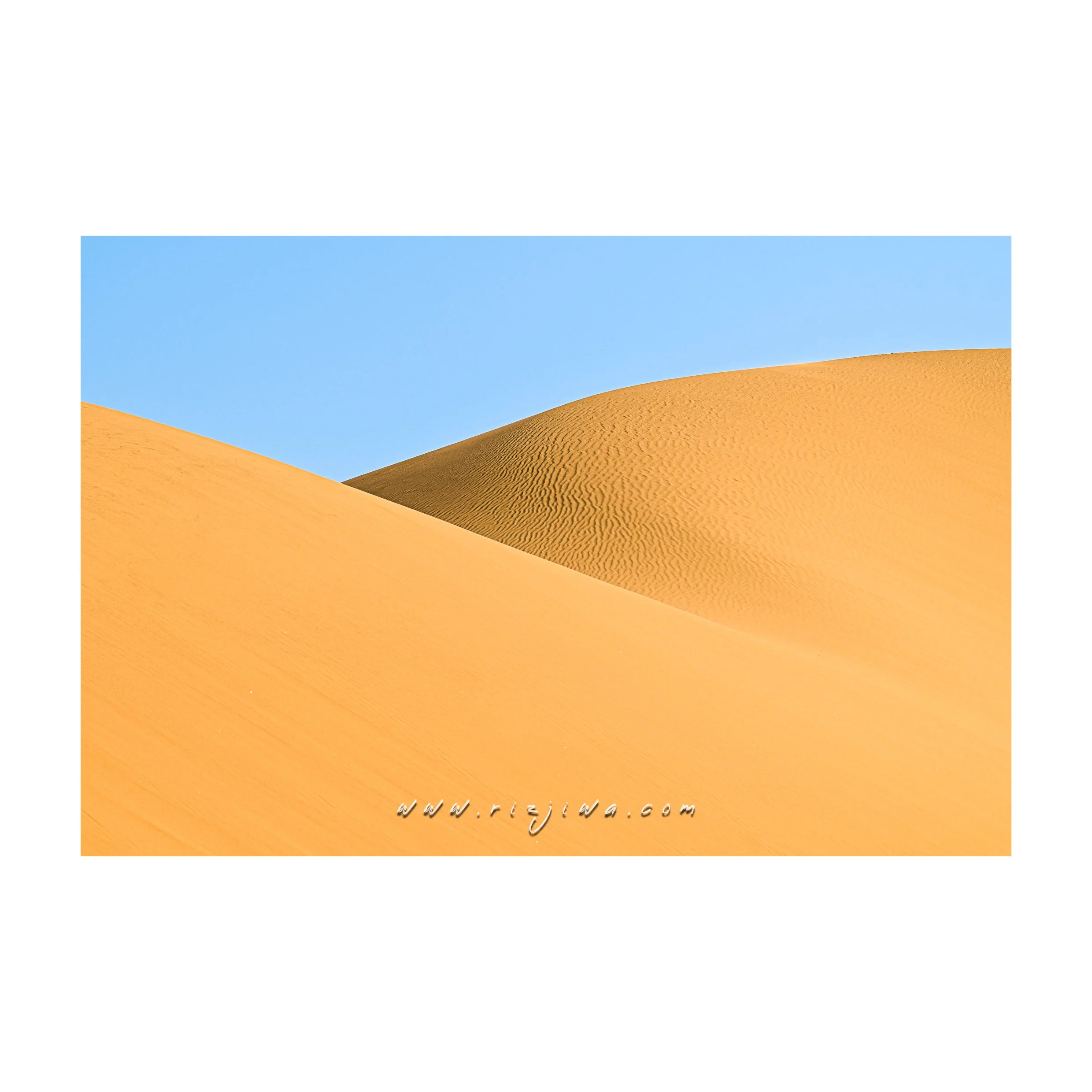 Sand dunes under a clear blue sky, showing smooth and rippled textures.