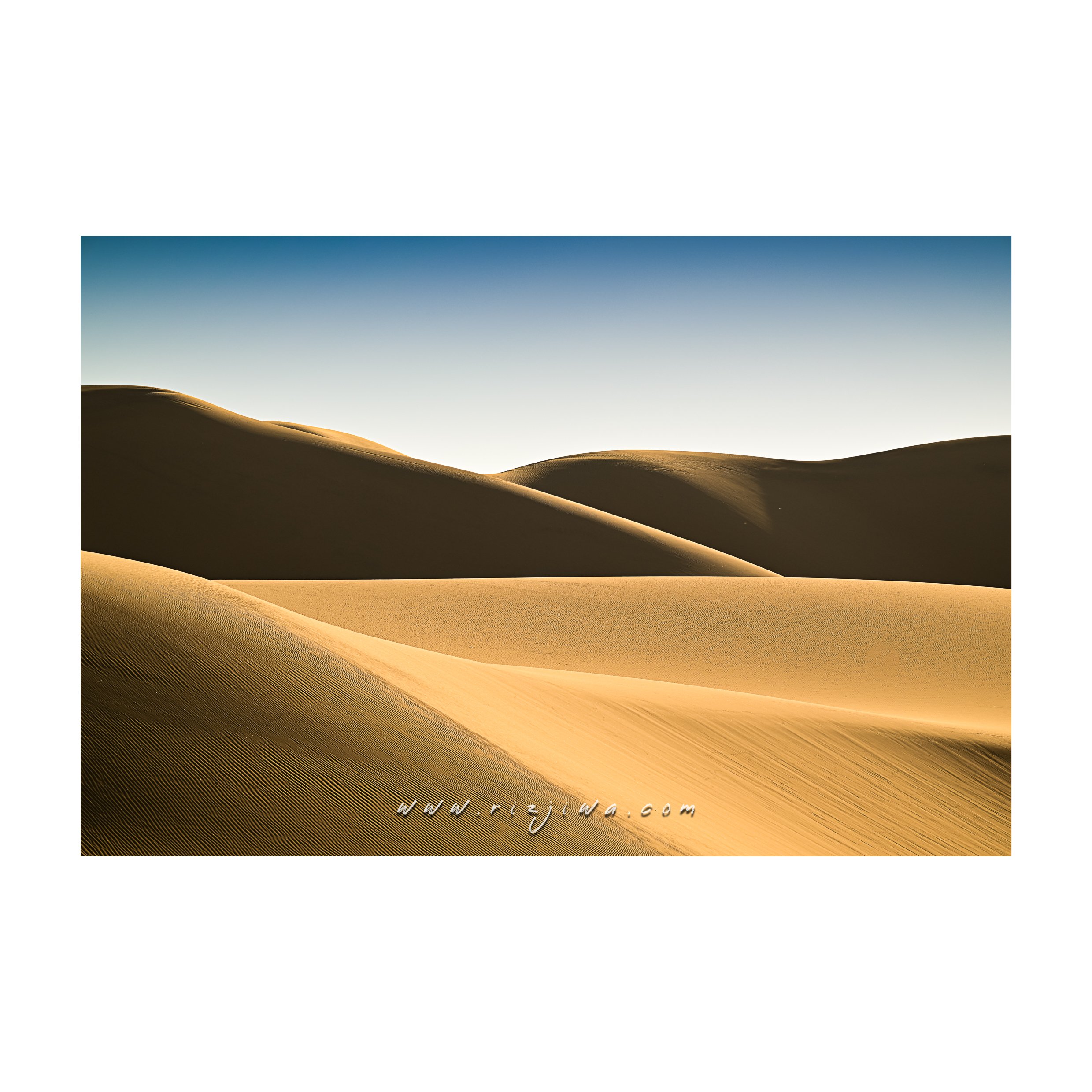 Sand dunes in a desert with a clear blue sky.
