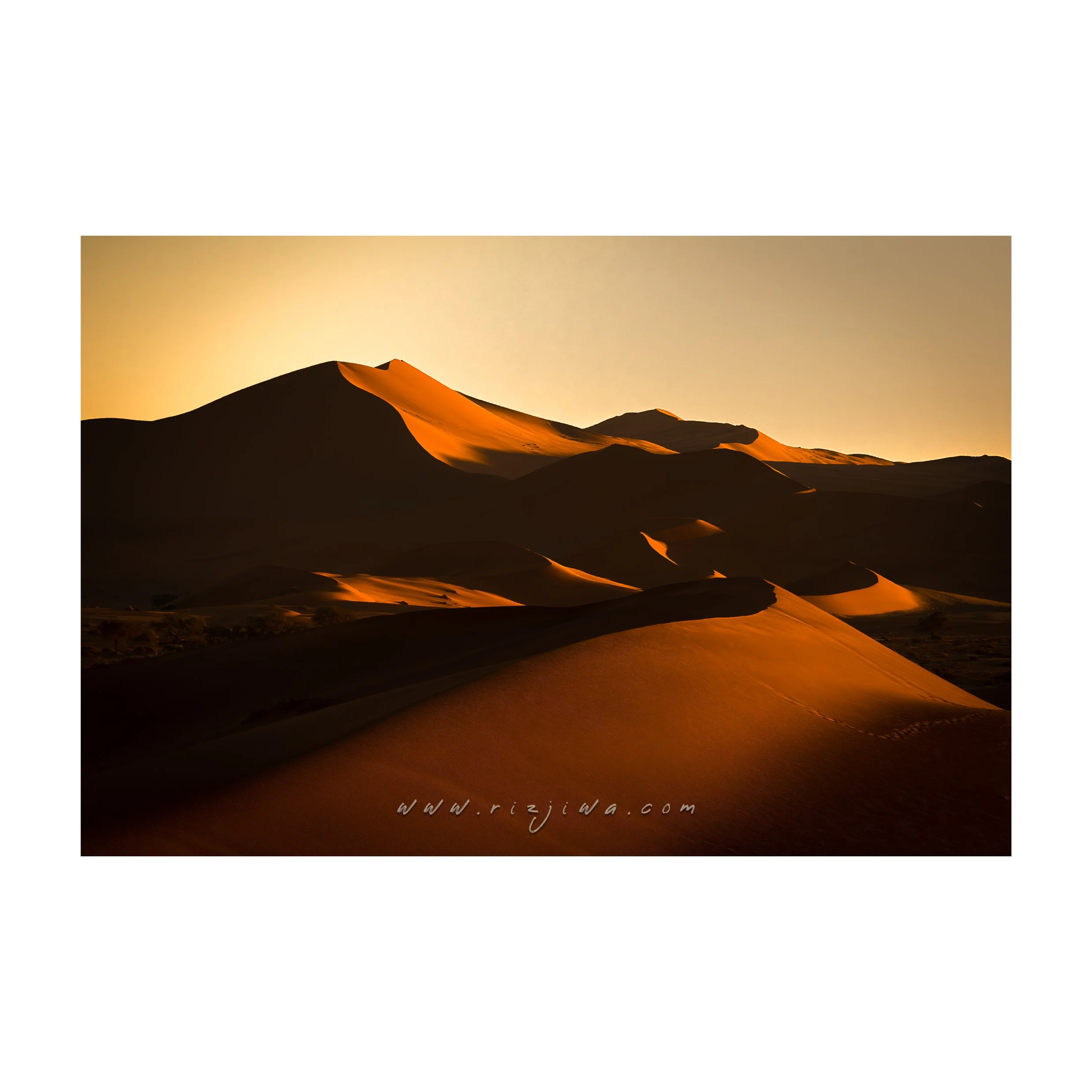 Sand dunes in a desert at sunset with a clear sky.