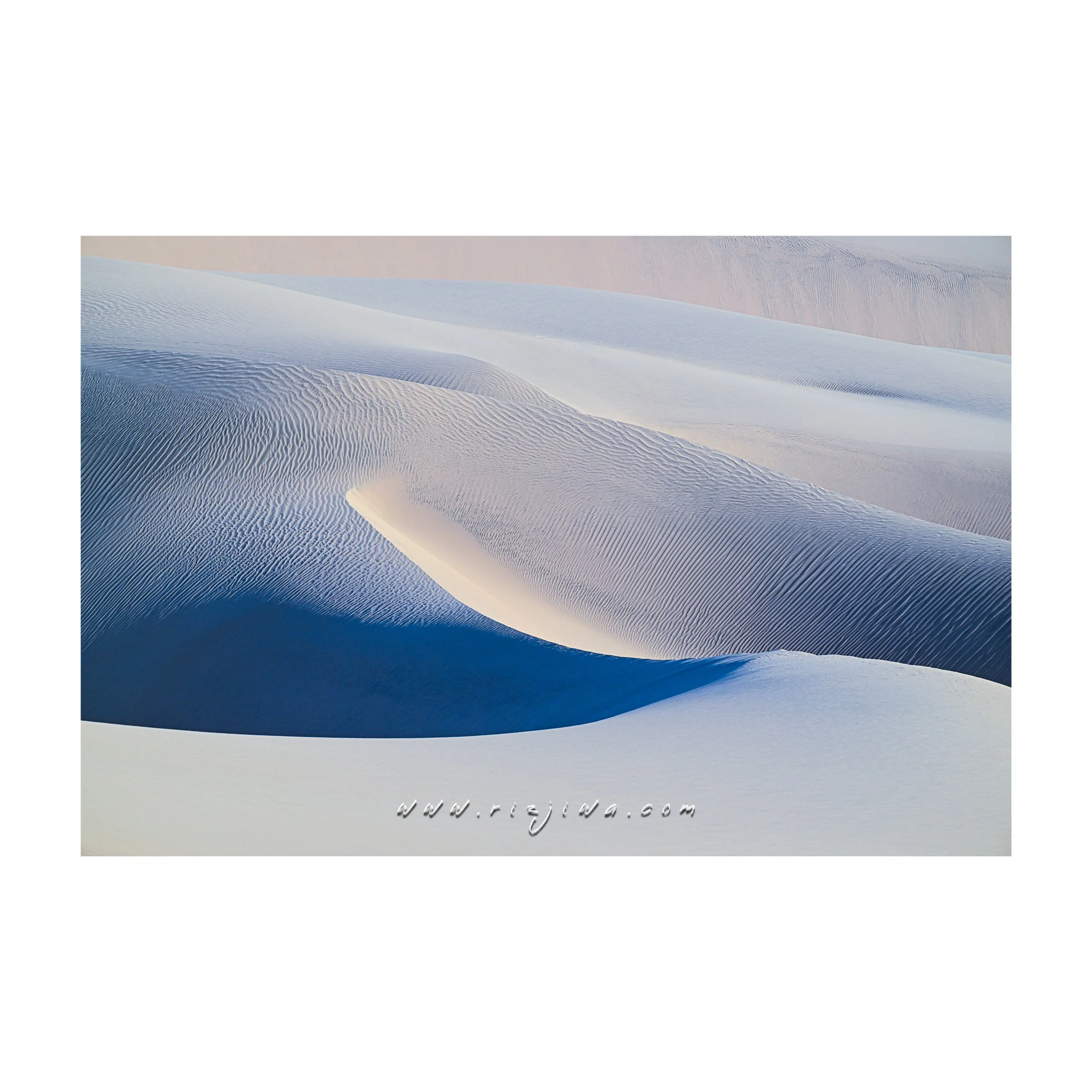 Sand dunes in a desert with smooth, rippled patterns and gentle curves in shades of white and blue.