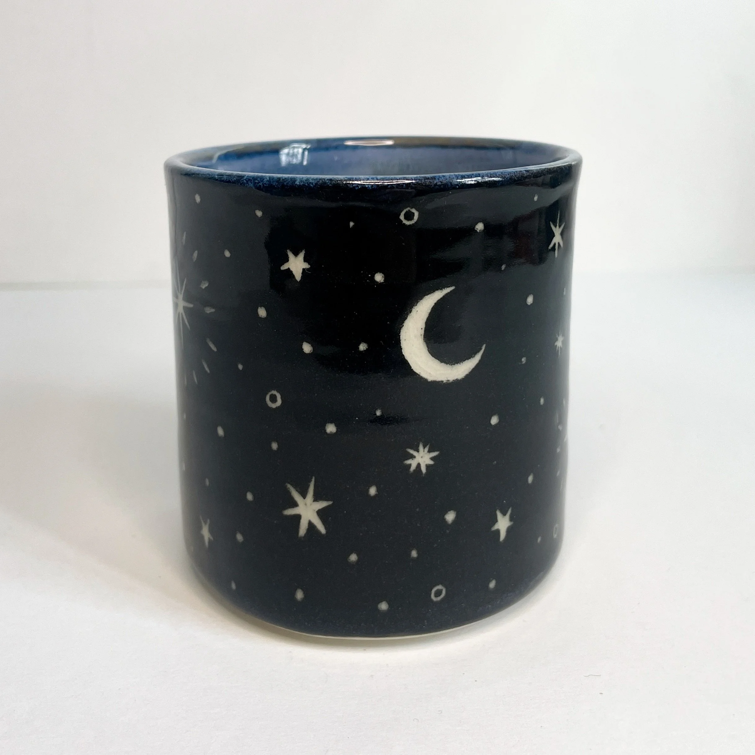 a black ceramic cup with a white moon and stars on the exterior. the interior is blue.