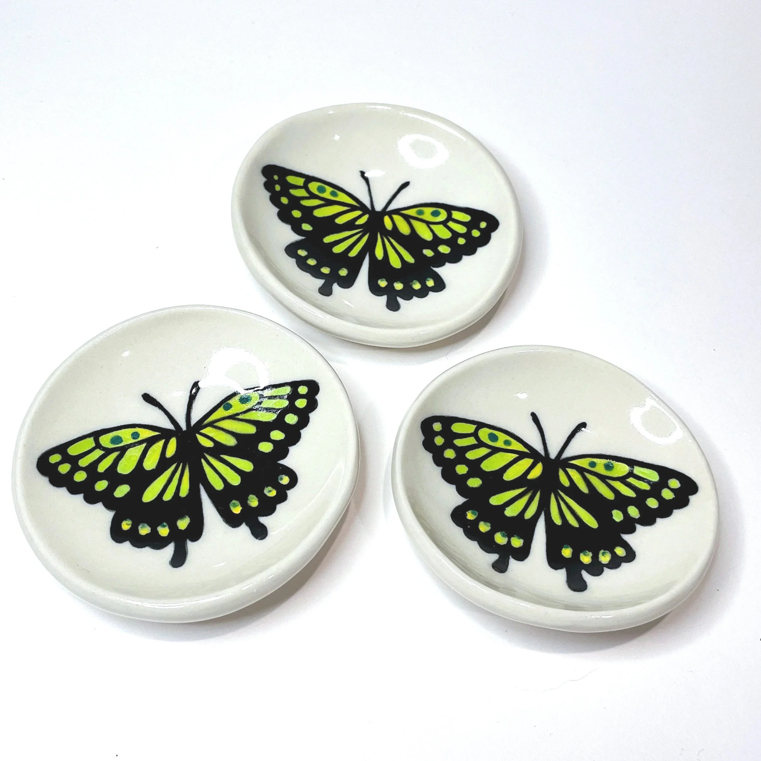 three small ceramic dishes with a green and black butterfly on each one..