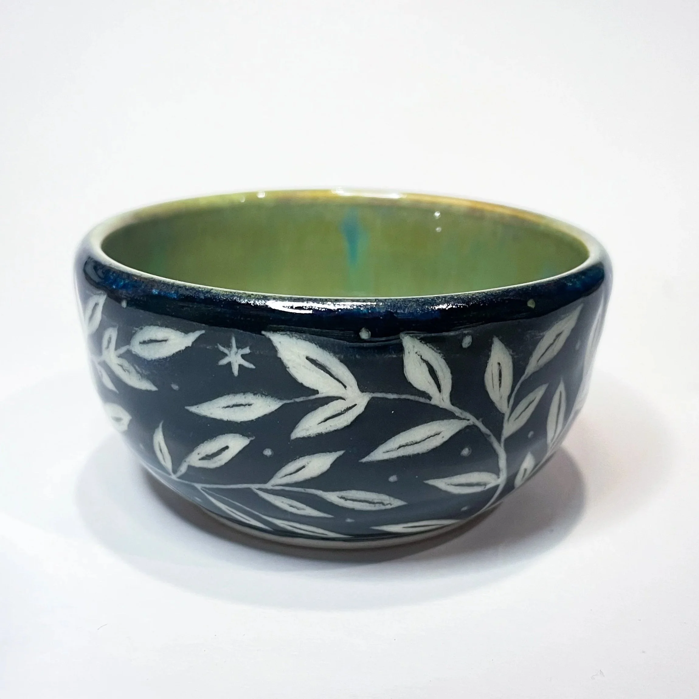 A small, black, ceramic trinket bowl with white leaves and stars wrapping around the exterior. The interior is green.