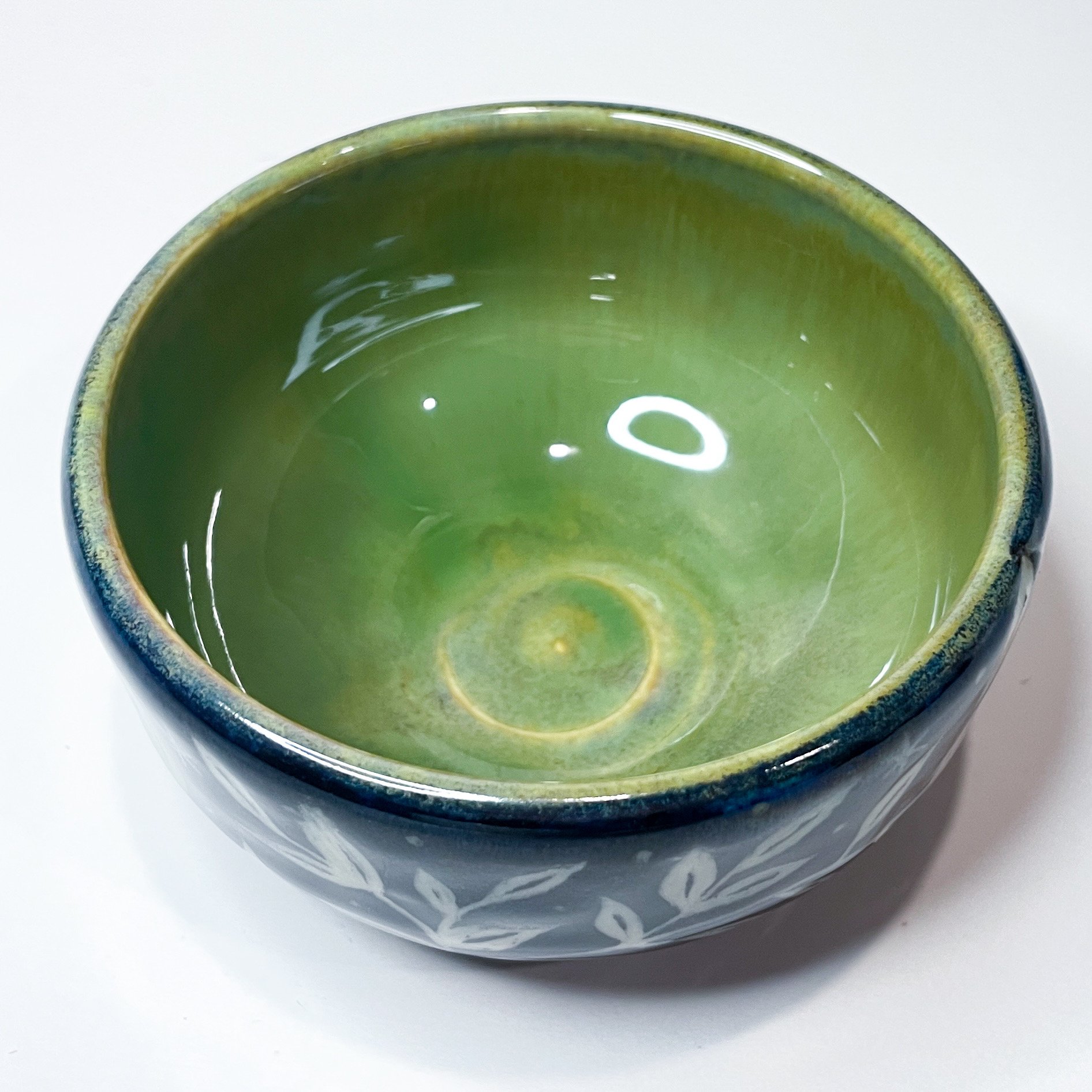A small, black, ceramic trinket bowl with white leaves and stars wrapping around the exterior. The interior is green.