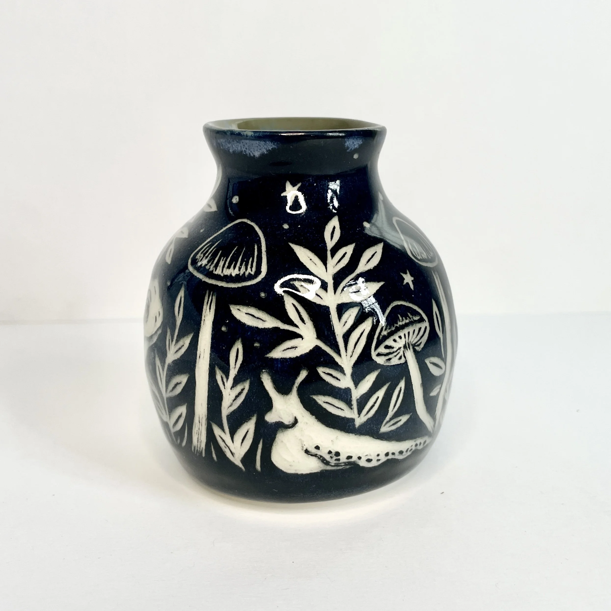 a small ceramic bud vase. the exterior is black and has a white slug and leaves. the interior has green around the rim.