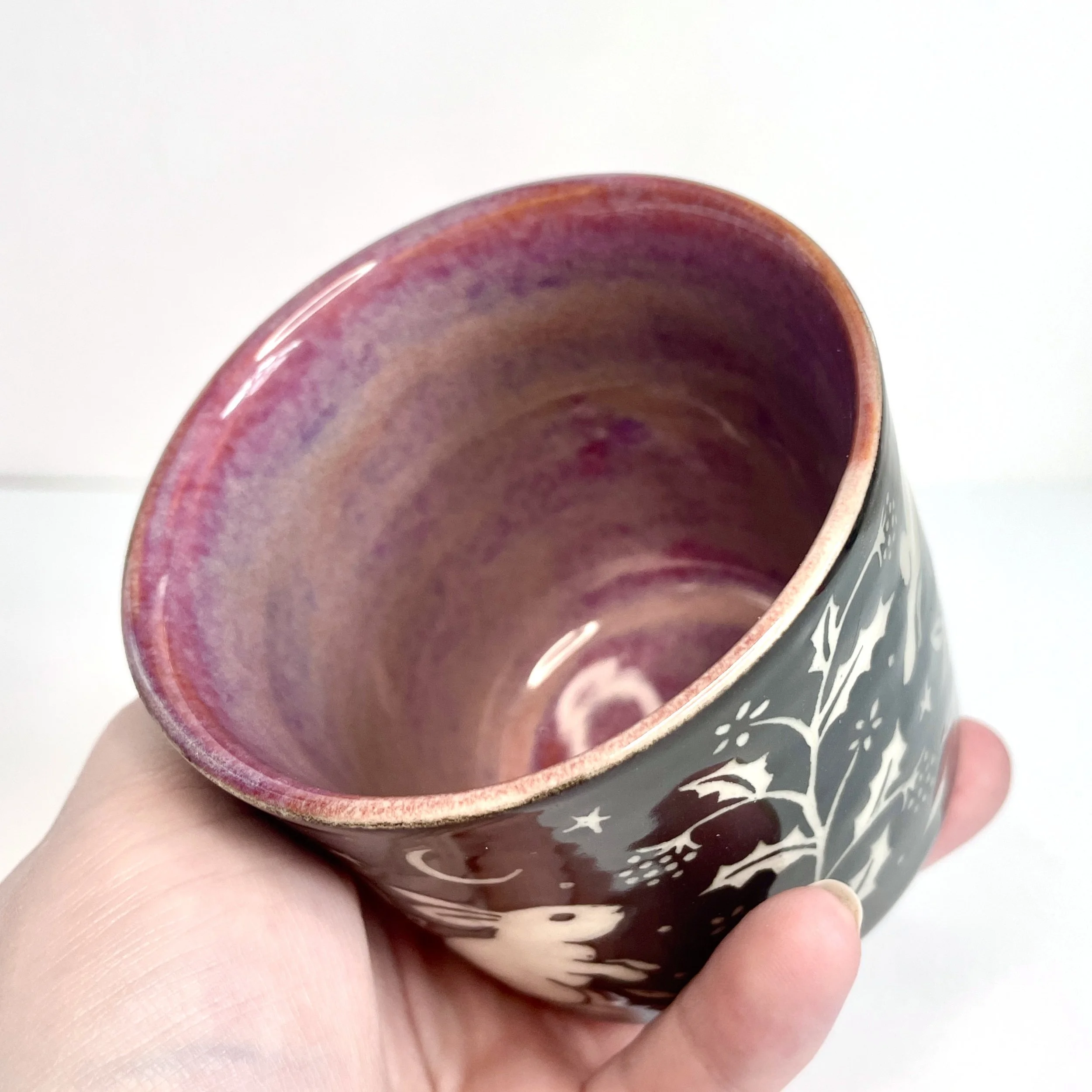 a ceramic cup. The exterior is black and has white bunnies, stars, and leaves. The interior is pink.
