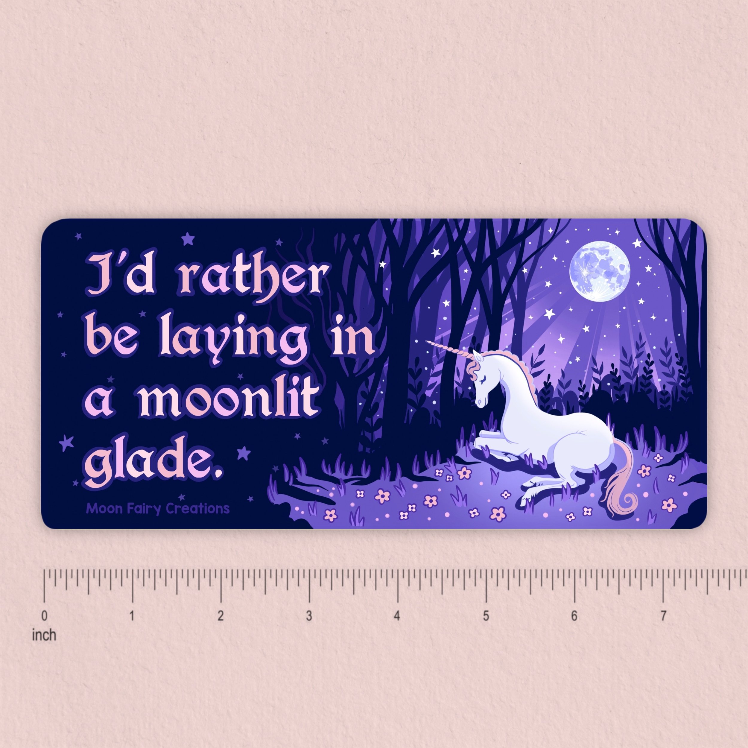 Bumper sticker that says "I'd rather be laying in a moonlit glade" with a unicorn laying in a purple moonlit forest with a ruler showing it is 7.5 inches wide.