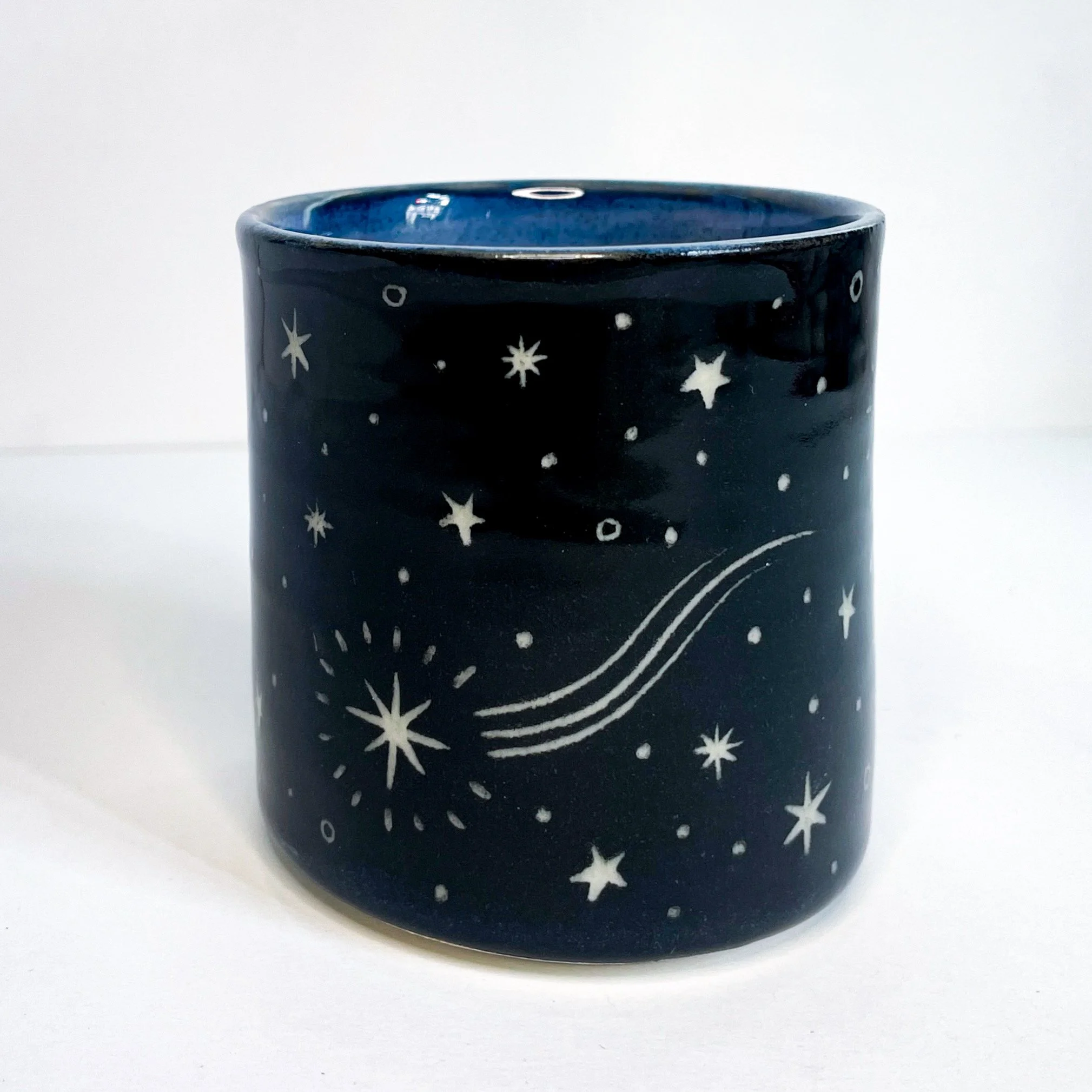 a black ceramic cup with a white stars on the exterior. the interior is blue.