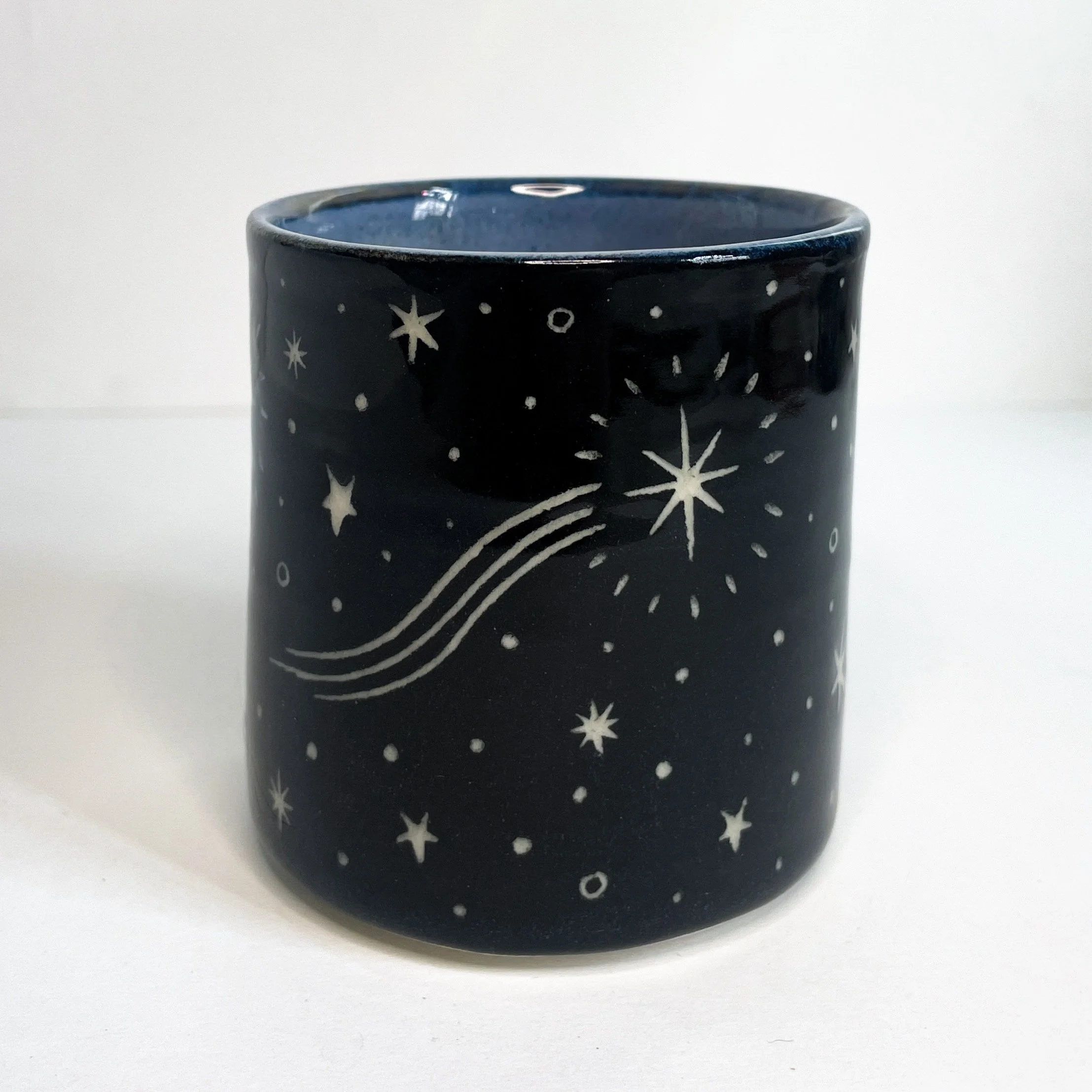a black ceramic cup with a white moon and stars on the exterior. the interior is blue.