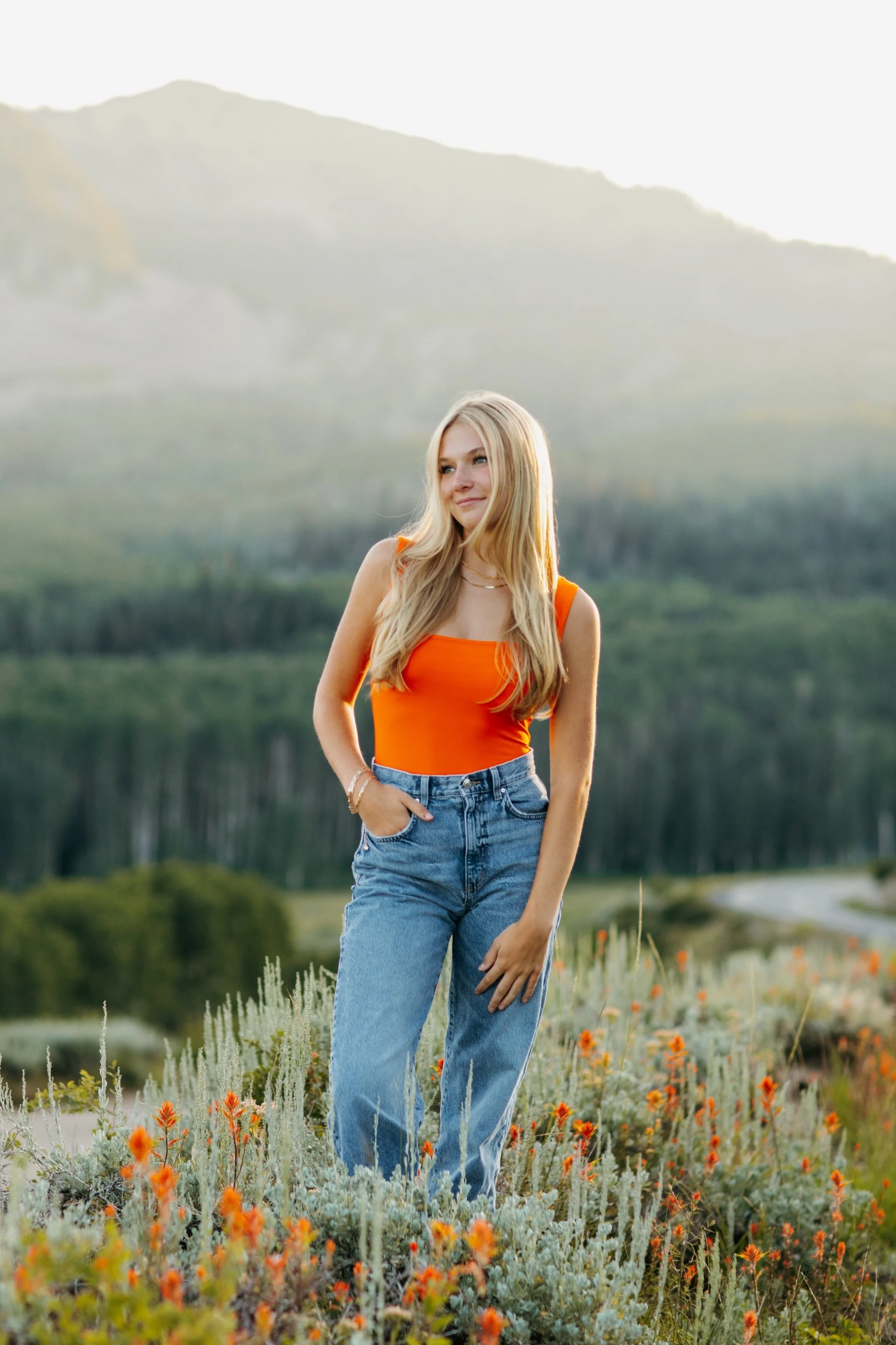 High school senior standing in a wildflower field in the mountains, wearing denim jeans and a neon orange shirt. Park City Utah Senior Photos. Digital and 35mm film photography.