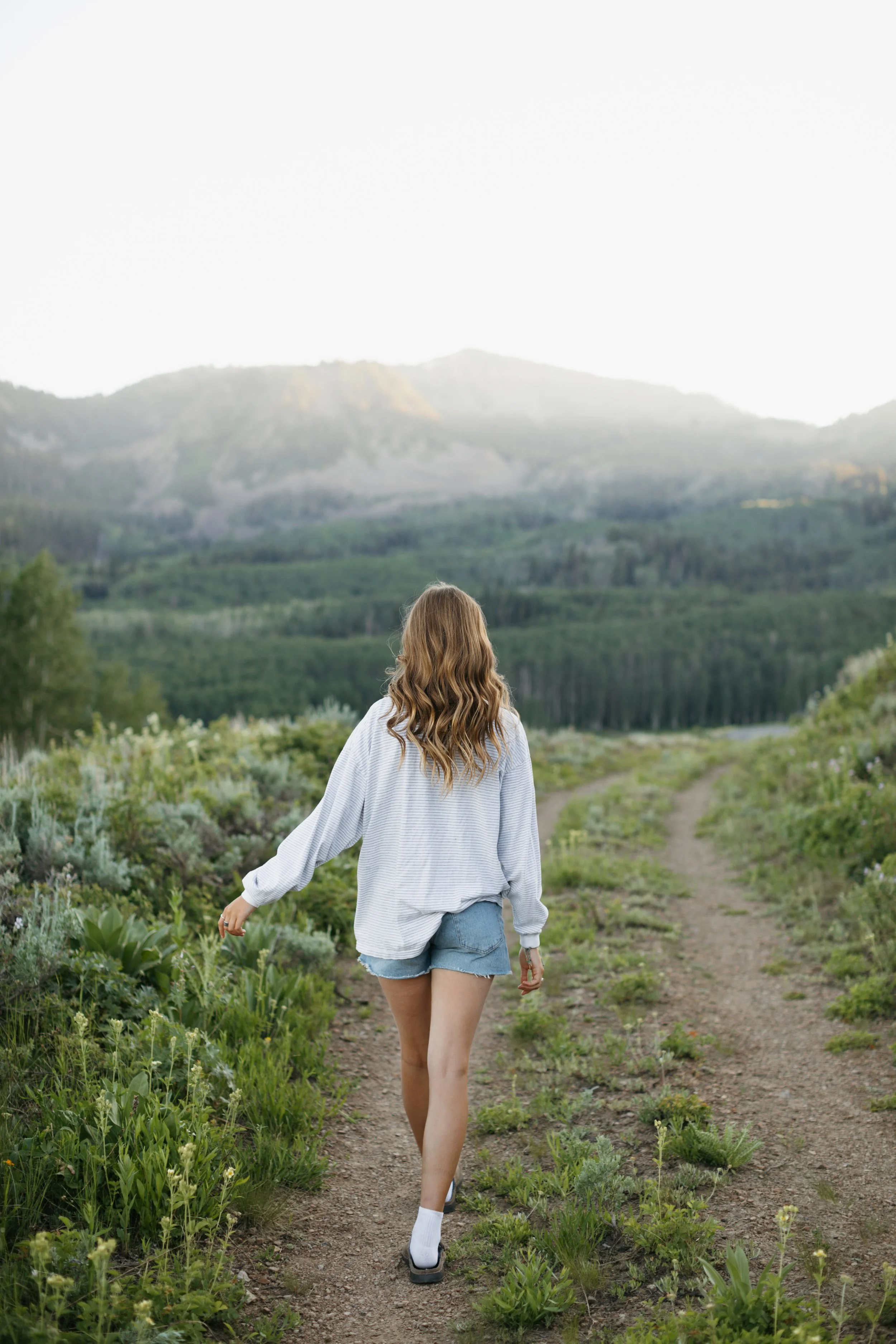 High school senior walking away from the camera on a trail with a mountain sunset in the background. 35mm film and digital photography. Park City Utah.