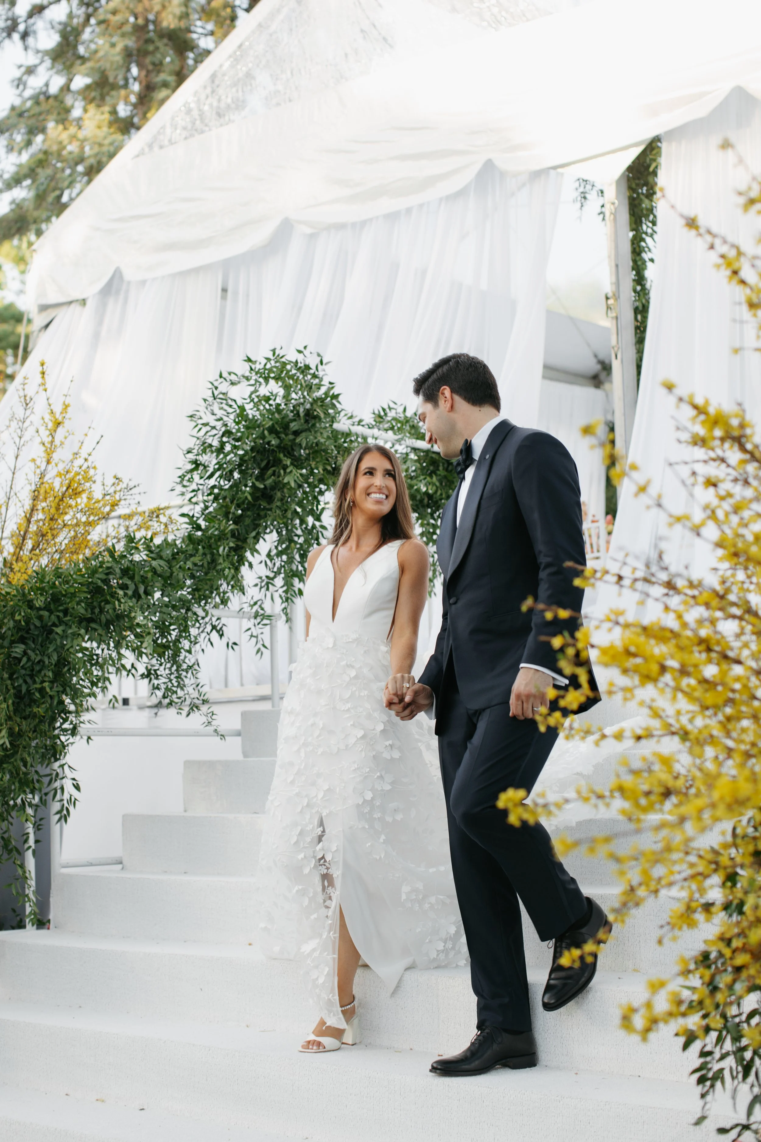 Bride and groom walking down a set of white stairs while yellow flowers and greenery decorate the railings. Digital and 35mm film Minneapolis Minnesota Wedding Photographer.
