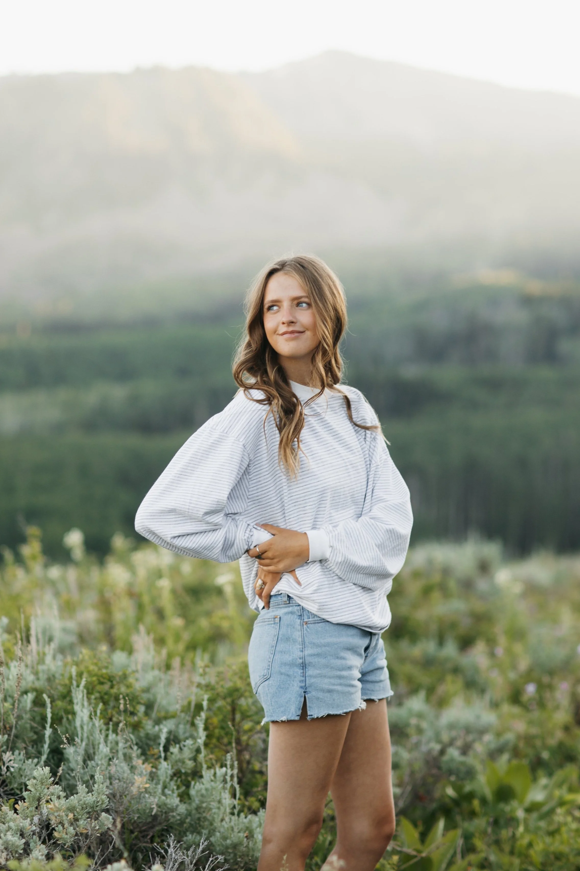 High school senior standing in a wildflower field with her hand on her hip, looking to her right, with a sunset Mountain View behind her. Park City Utah Wedding and Portrait Photographer. 35mm film and digital photography.