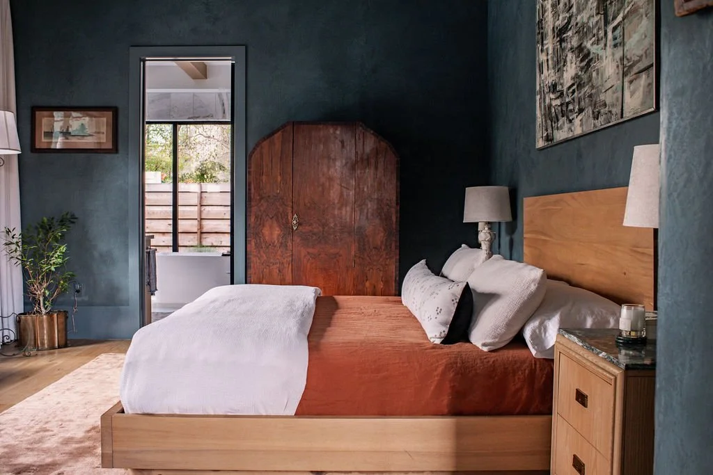 Bedroom designed by Faust House Studio in Austin, with dark teal walls, a wood bedframe, and warm layered bedding.