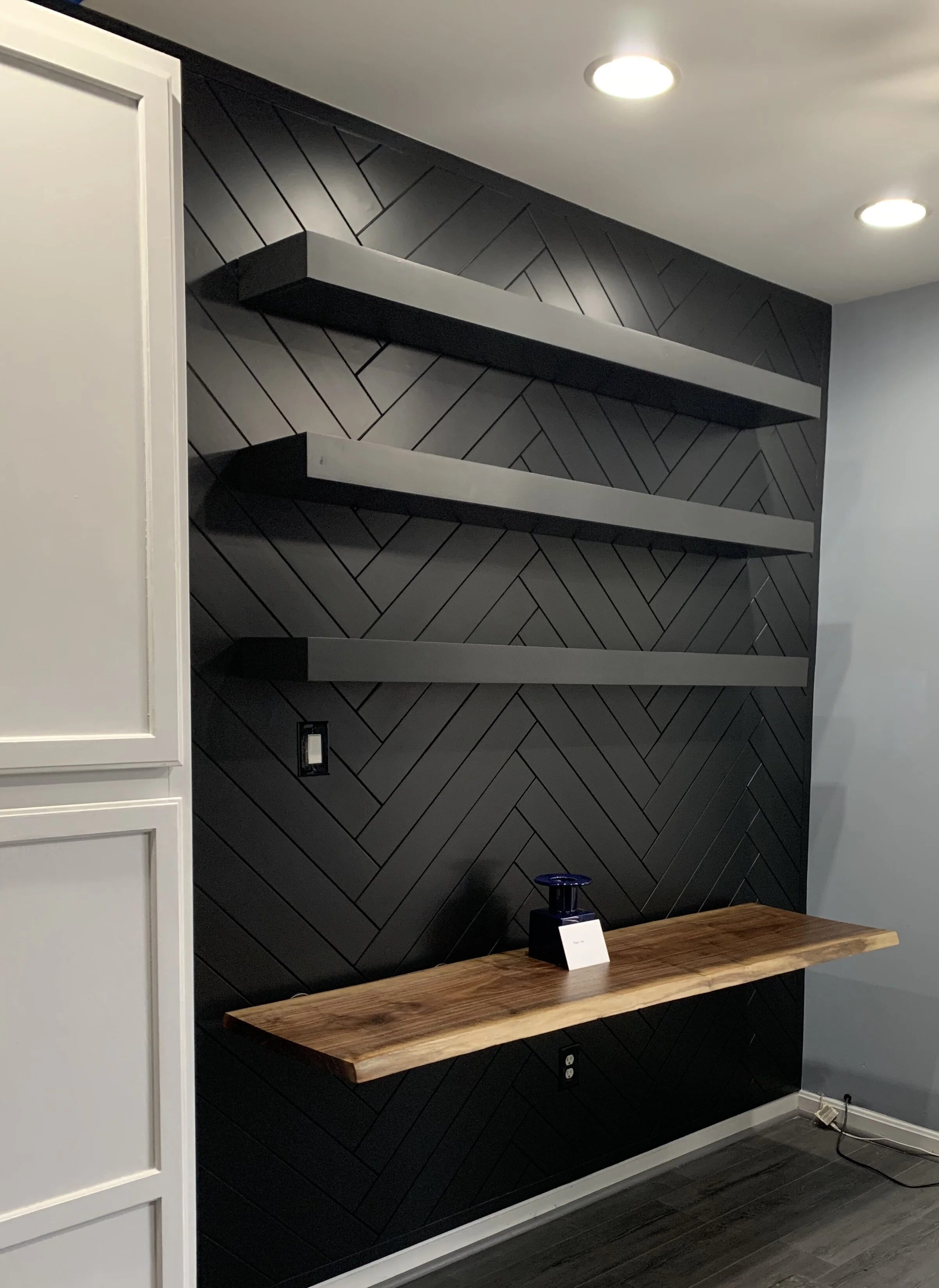 Herringbone wall with custom floating shelves and live edge wood slab for floating desk.