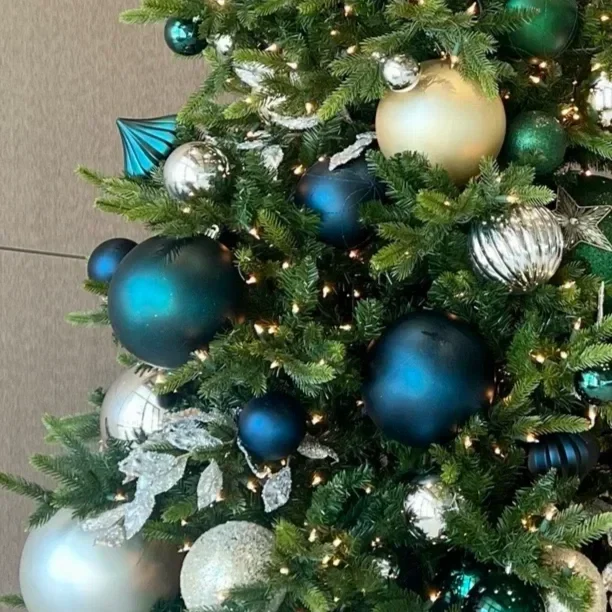 Close-up of a decorated Christmas tree with green branches, gold and teal ornaments, and small warm white lights.