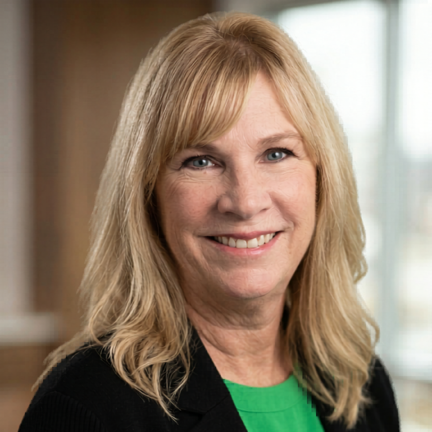 A woman with blonde hair smiling, wearing a red blouse, with a blurred green and yellow outdoor background.