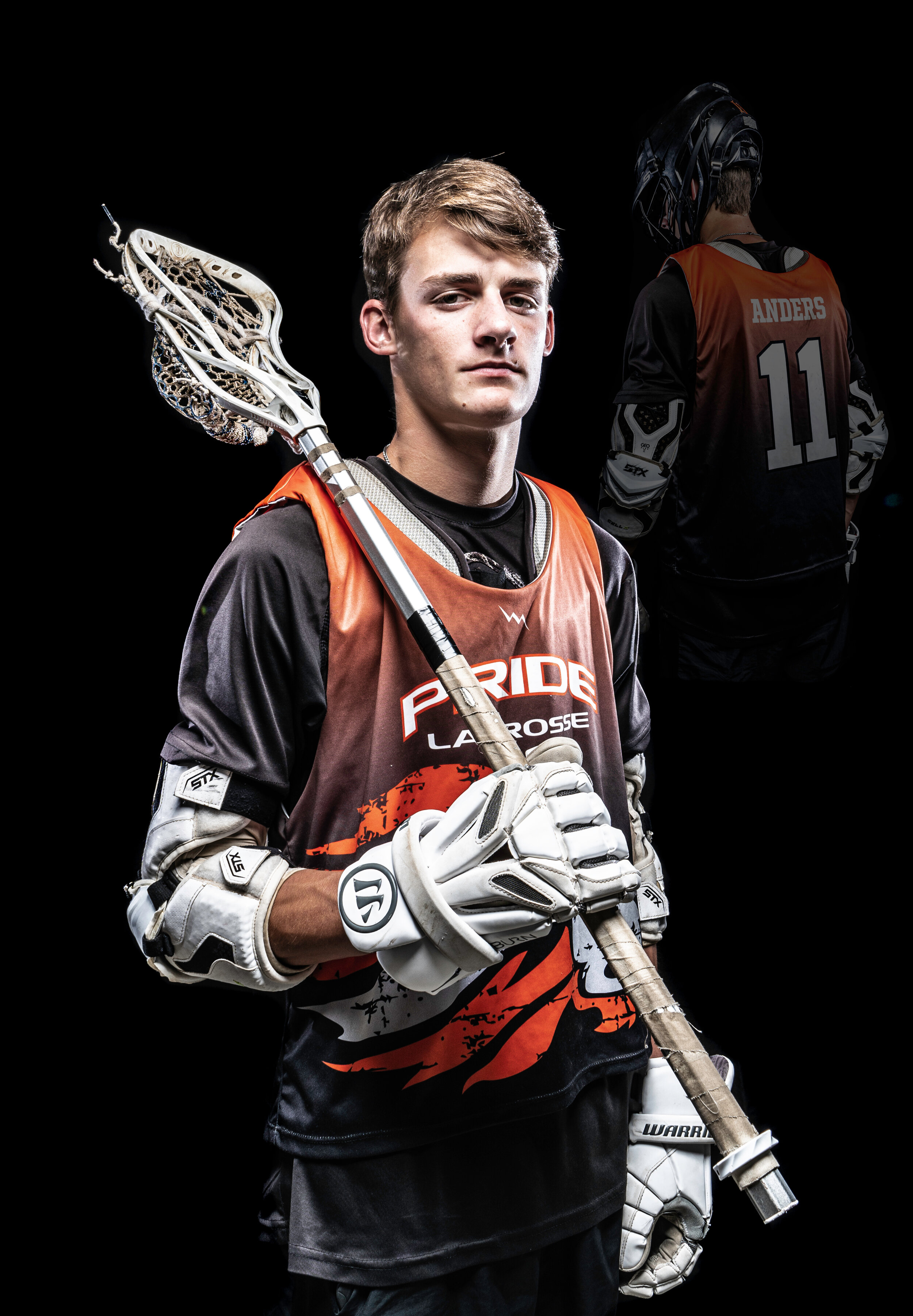Lacrosse player in uniform holding lacrosse stick, wearing protective gear, black background.
