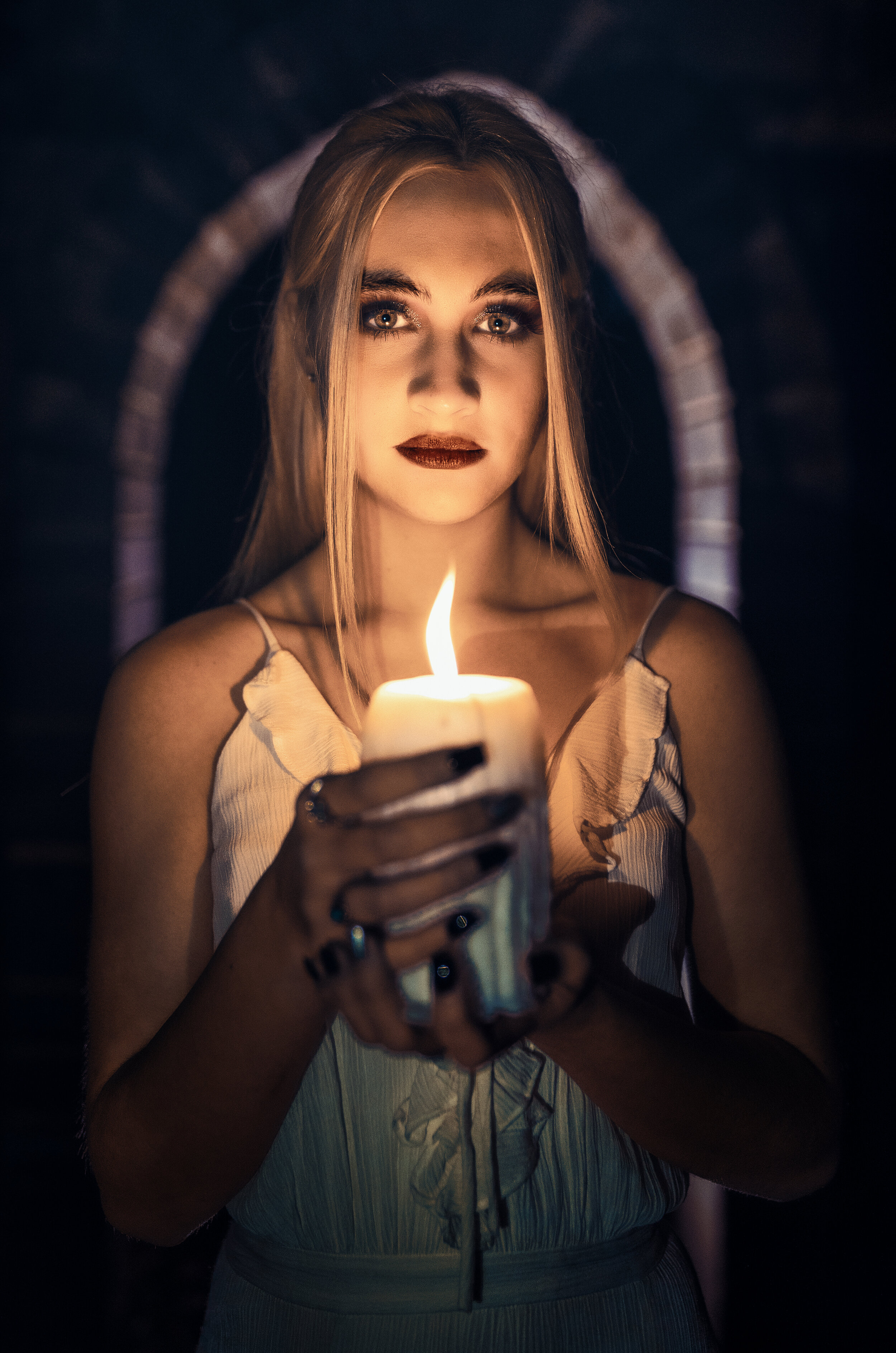 Woman in dark holding a lit candle, with a focused expression, wearing a light-colored dress.