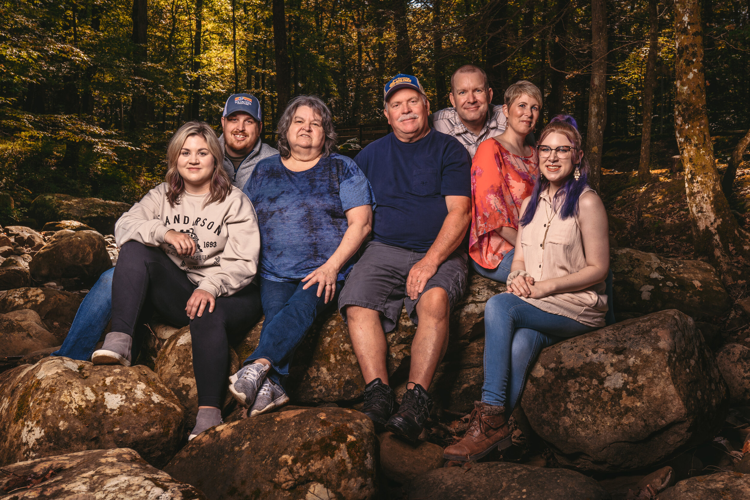 A group of people posing together outdoors on rocks in a forest.