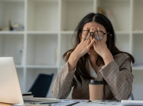Woman sitting at a desk holding her head, showing stress or jaw tension - TMJ Treatment in Westfield, IN