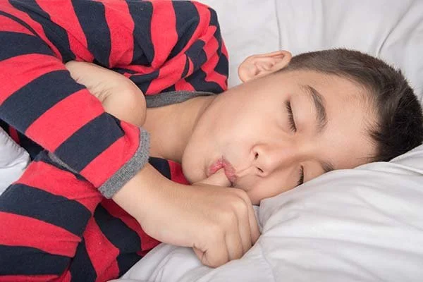 Child lying in bed sucking thumb, showing dental effects - Overbite vs. Underbite in Westfield, IN
