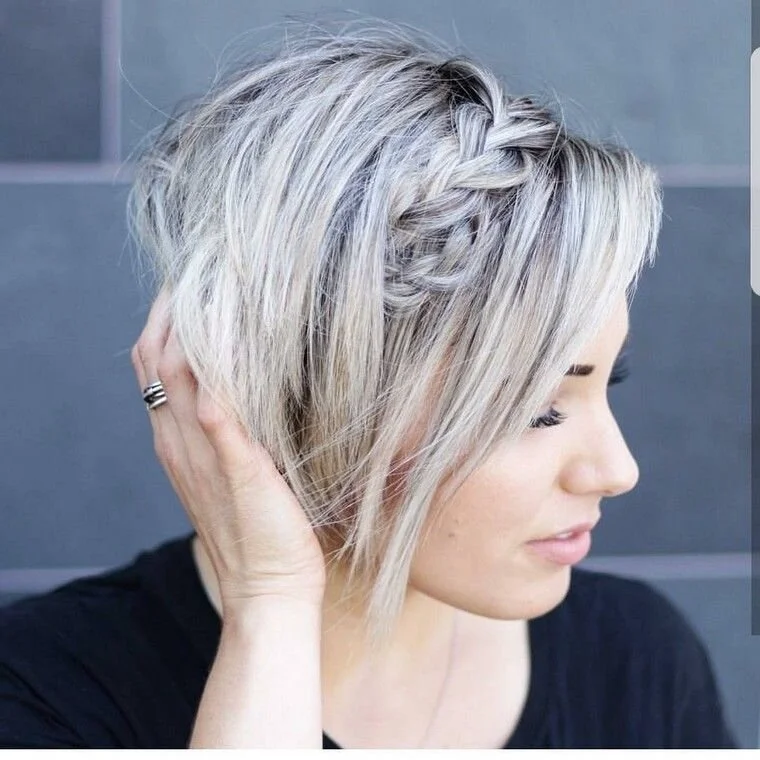 Jeune femme aux cheveux blonds courts, avec une tresse sur le côté, berbée de cheveux en désordre et portant une robe noire, qui regarde vers la droite.