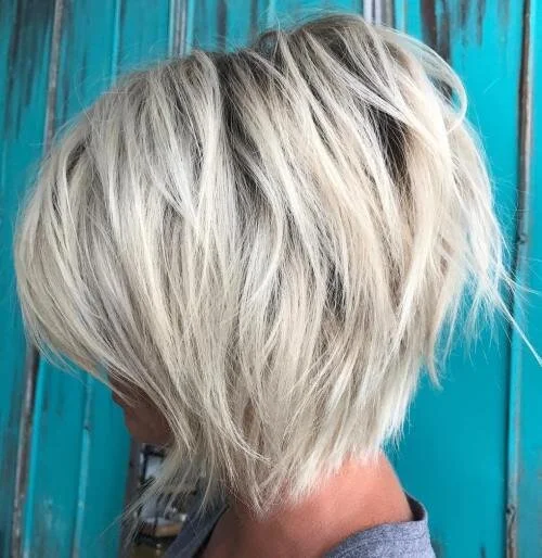 Photo d'une coupe de cheveux courte, blonde, et en désordre, avec une toile bleue en arrière-plan.