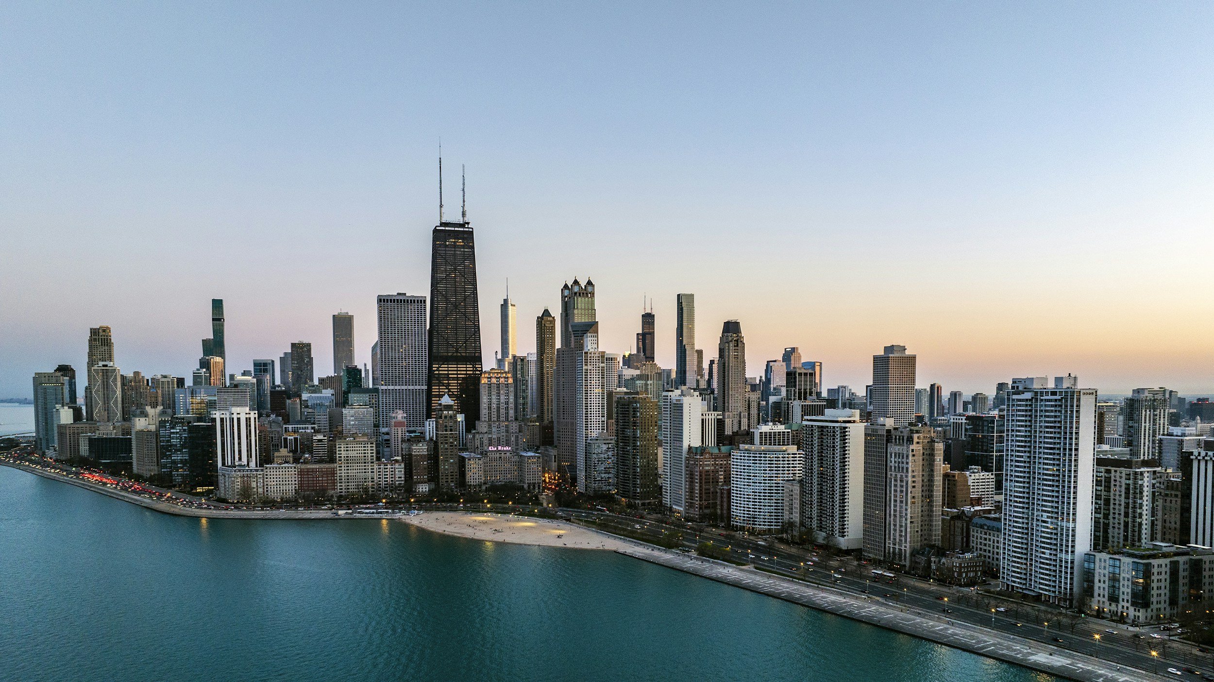 A panoramic view of Chicago skyline at sunset with tall skyscrapers, Lake Michigan, and a clear sky.