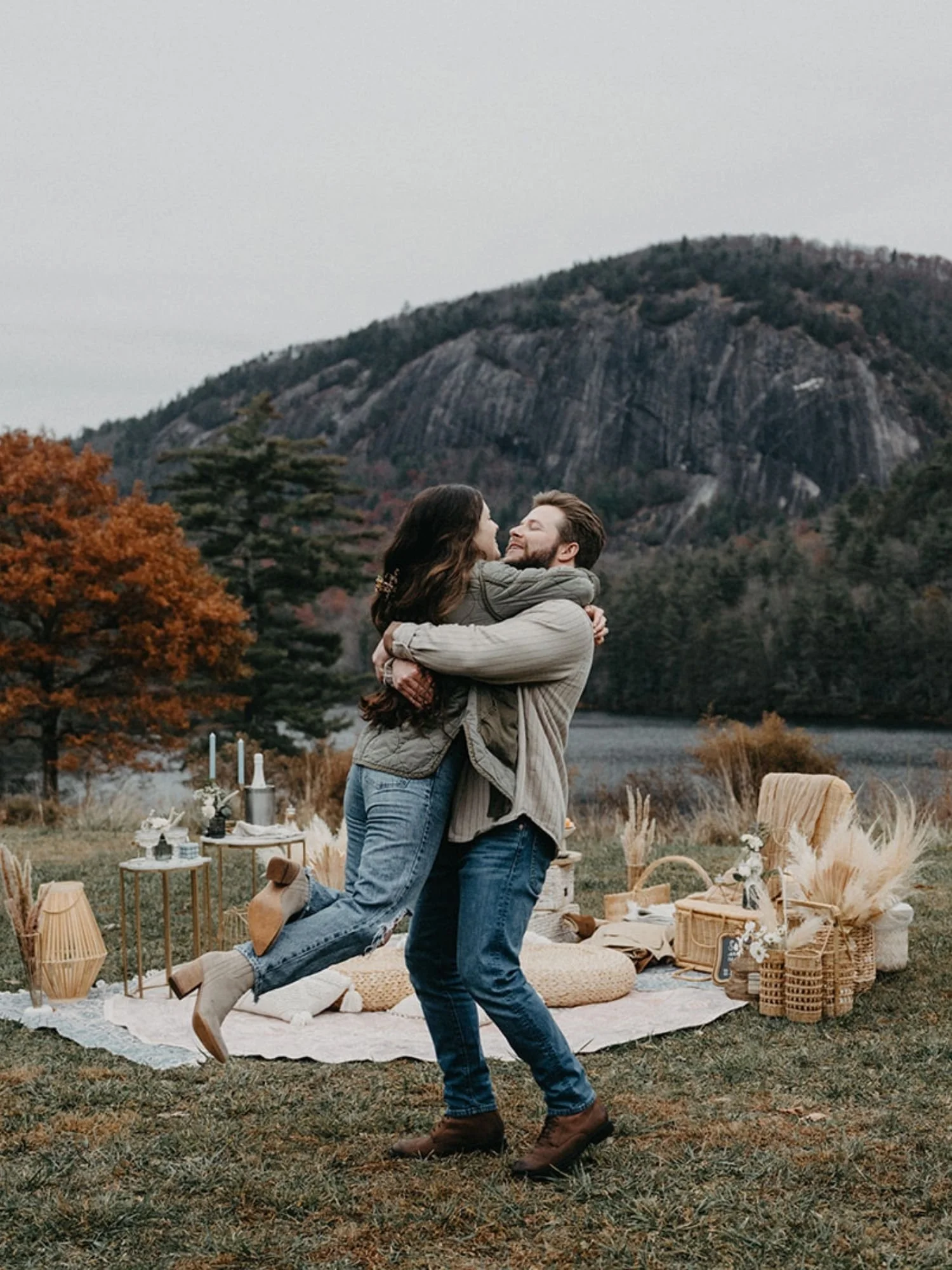 Couple celebrating their engagement at a mountain-view picnic setup near Asheville, surrounded by cozy neutral decor and scenic Blue Ridge backdrop.