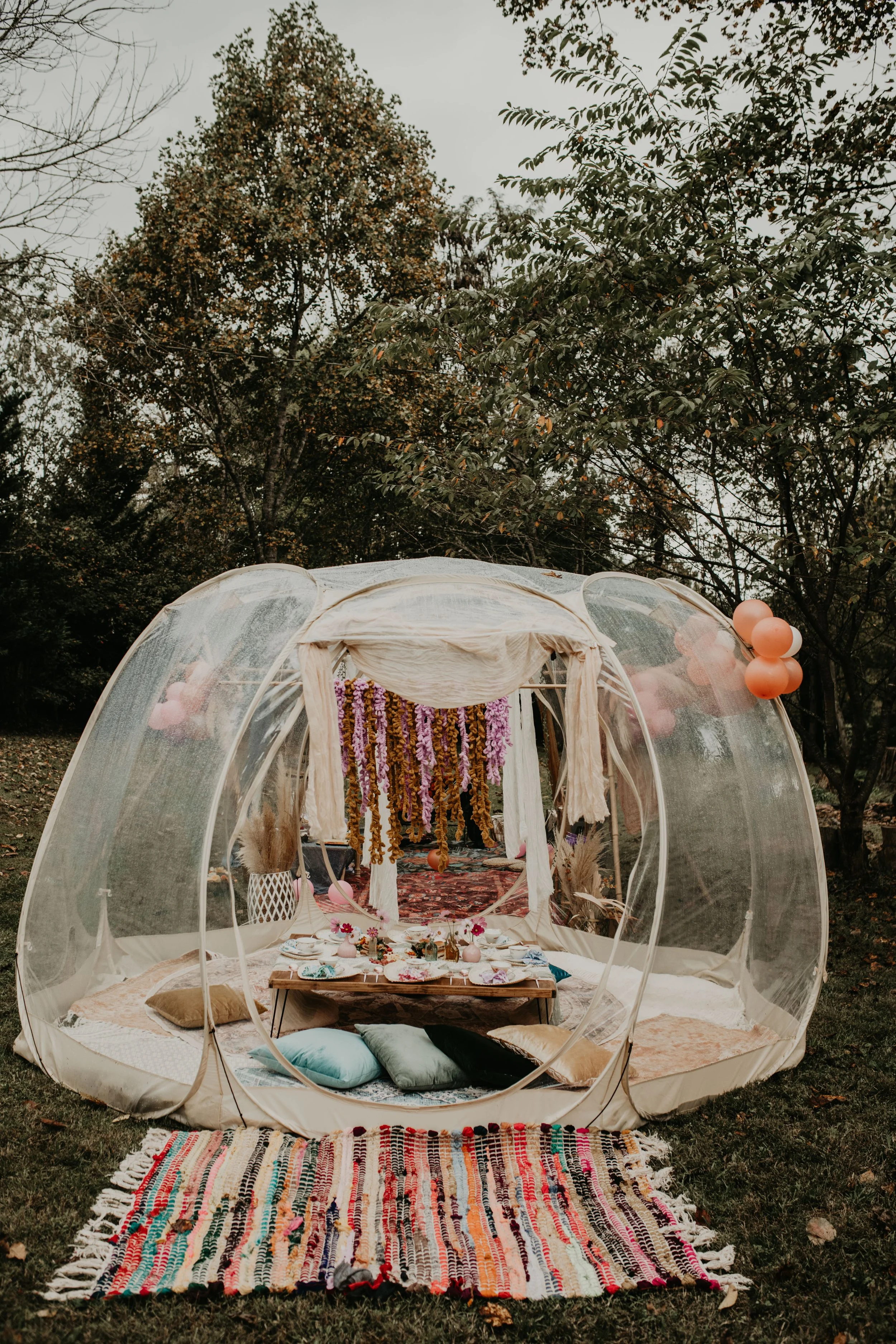 Outdoor kids tea party in Asheville featuring lace dome tent, balloon accents, rugs, and low picnic tables styled for a children’s birthday celebration.