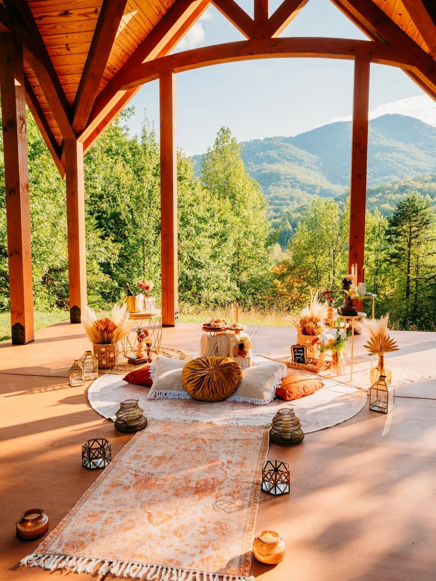 Luxury proposal picnic setup under a timber pavilion with mountain views in Asheville, featuring layered rugs, candles, pampas grass, and curated decor.