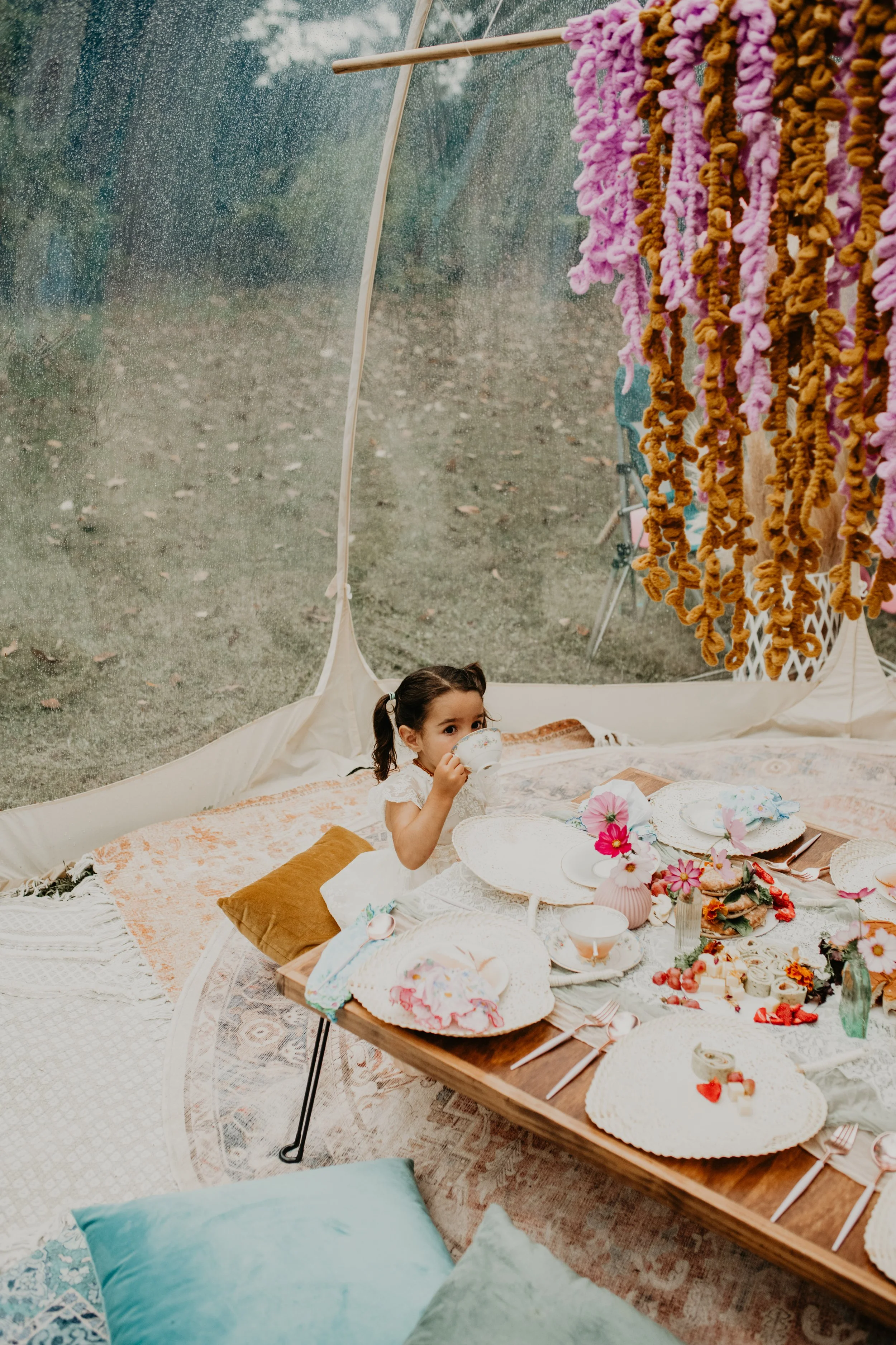 Young child sipping tea at a luxury kids tea party setup in Asheville with vintage teacups and soft picnic styling.