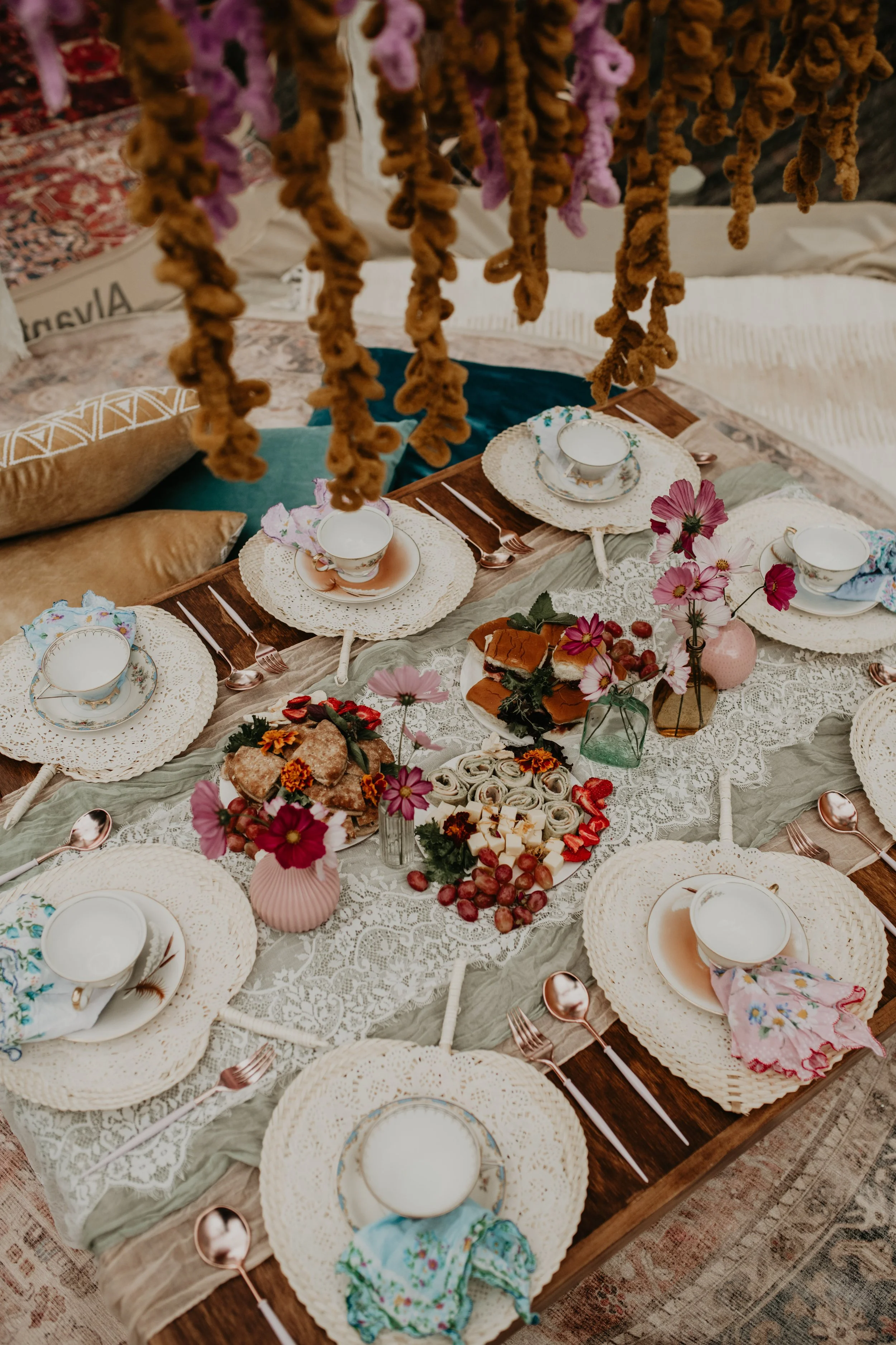 Elegant kids tea party table arrangement with teacups, cloth napkins, charcuterie snacks, and decorative florals for a birthday celebration.
