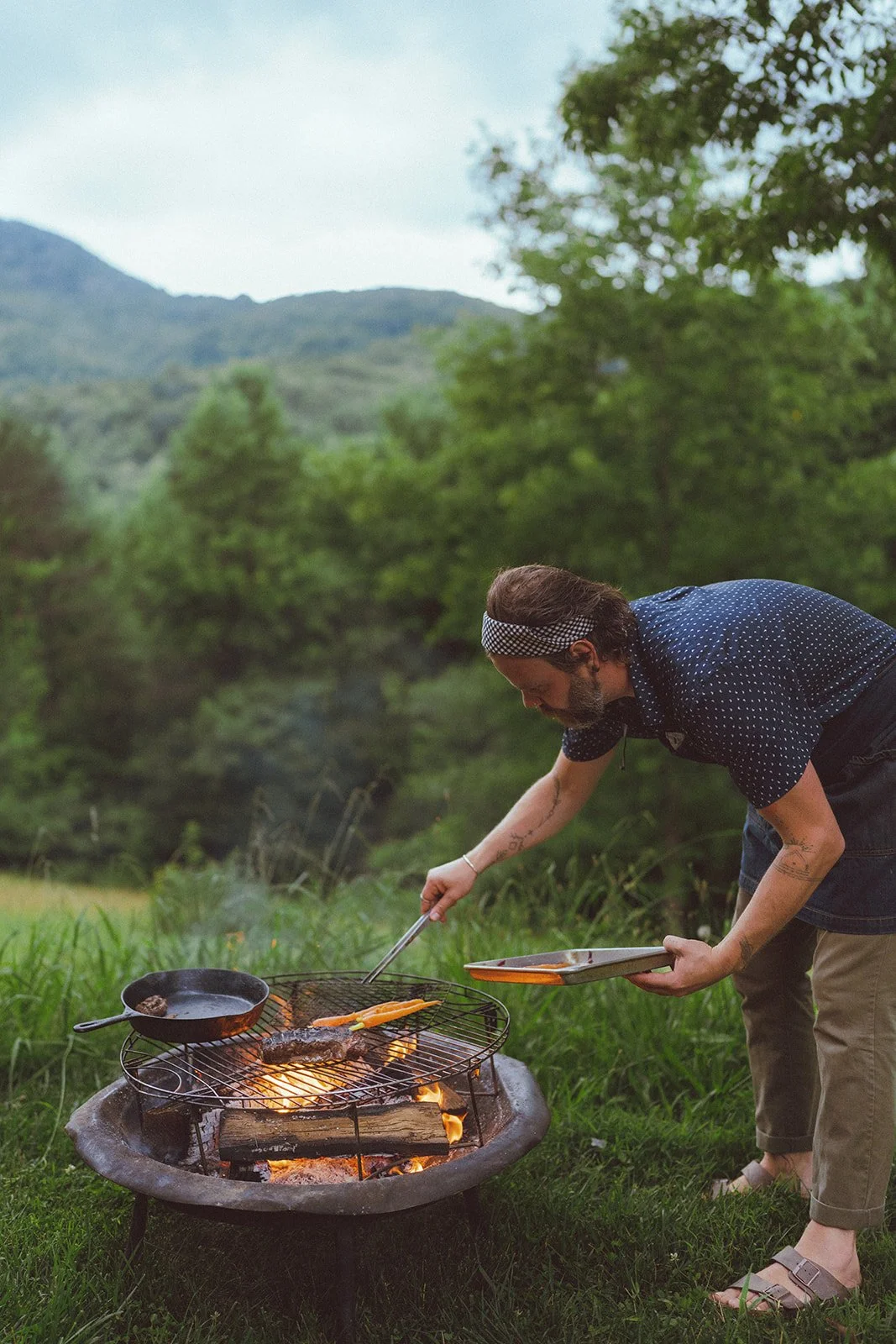 Private chef preparing an open-fire meal at a scenic outdoor location in Asheville, grilling over a wood fire as part of a luxury picnic dining experience.