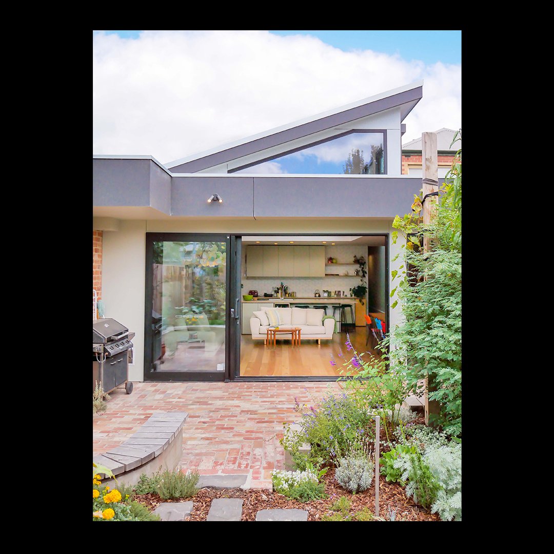 A light-filled living area is bought about by half vaulted ceiling, high windows, and sliding doors, allowing the transition between indoor and outdoor spaces to be seamless.